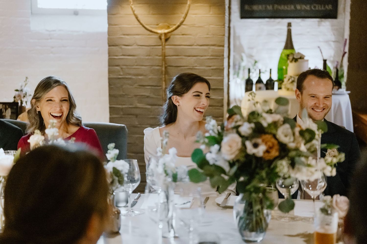 Candid laughter during a wedding reception dinner with beautiful floral arrangements.