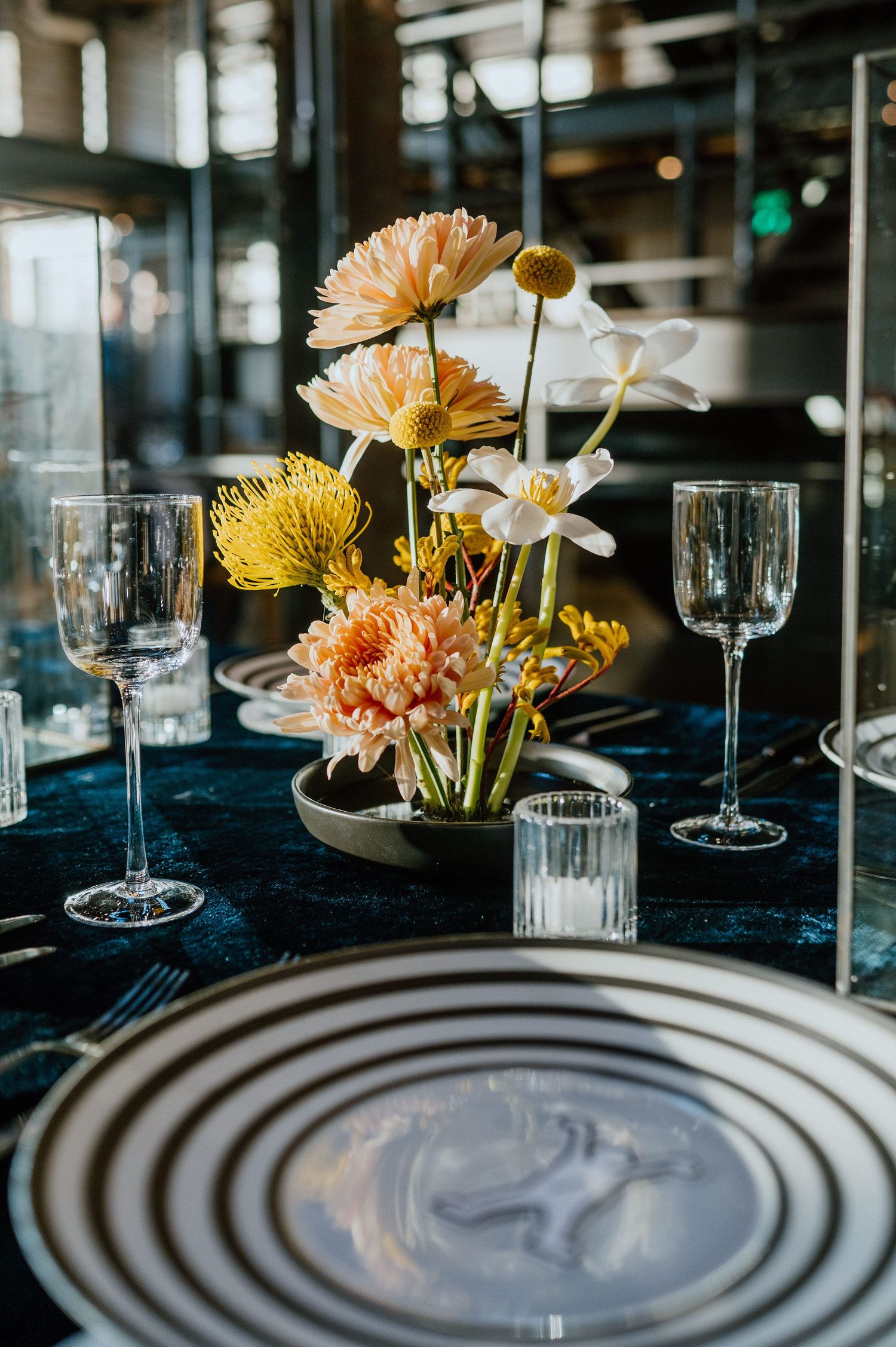 Yellow and peach floral centerpiece with striped plates on navy blue tablecloth.