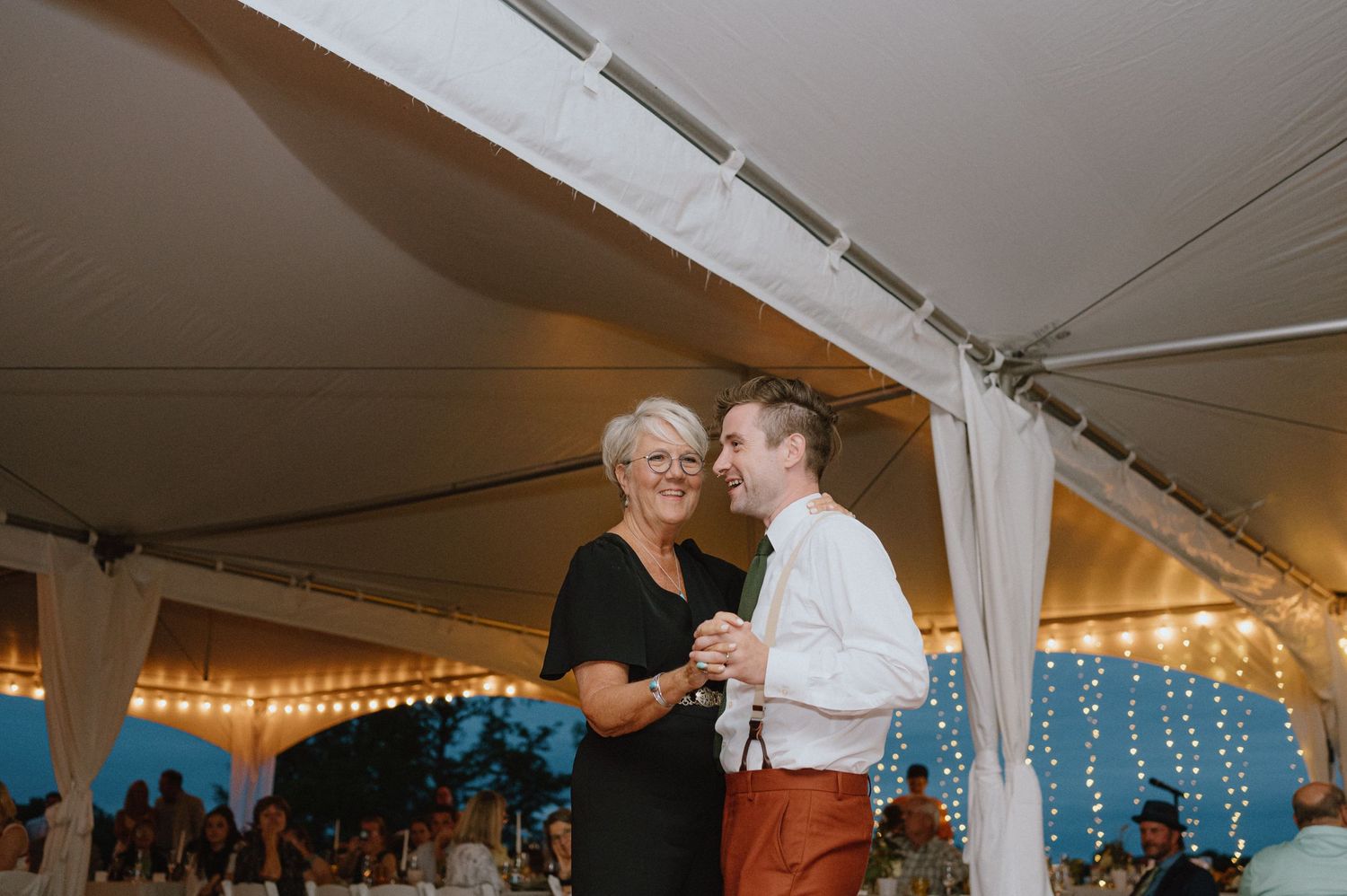 Emotional dance moment under reception tent with twinkle lights in background.