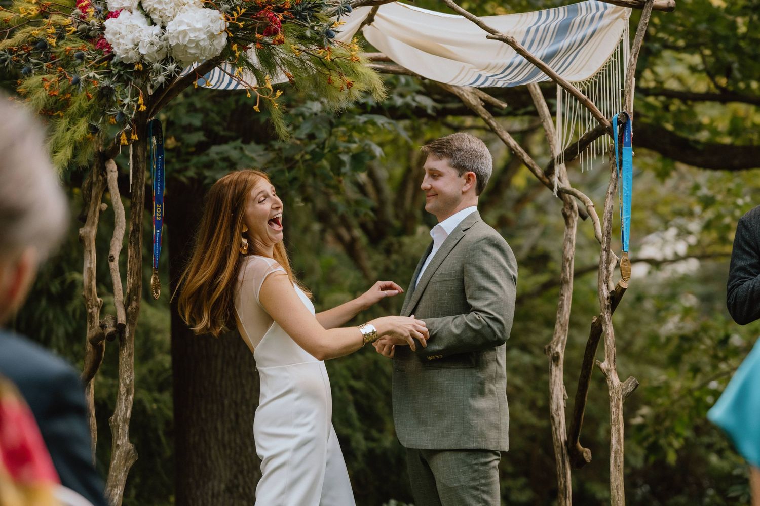 Wedding ceremony under rustic floral arch in outdoor forest setting.