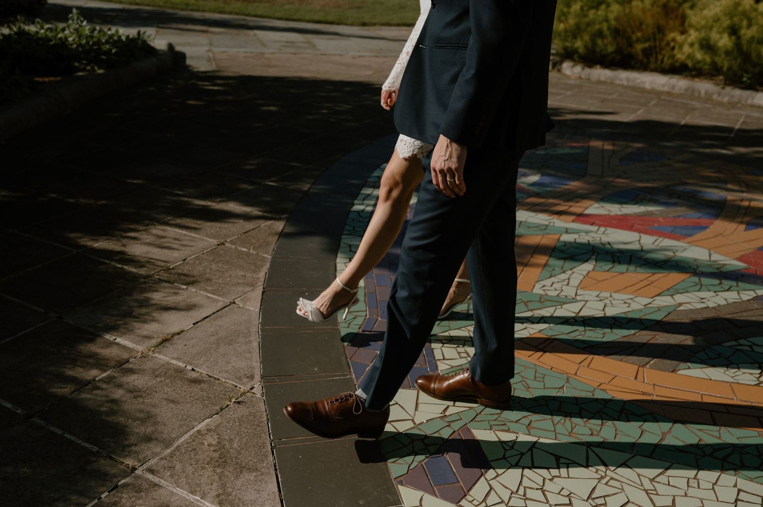 Cropped view of formal wear and shoes walking on decorative outdoor pavement.