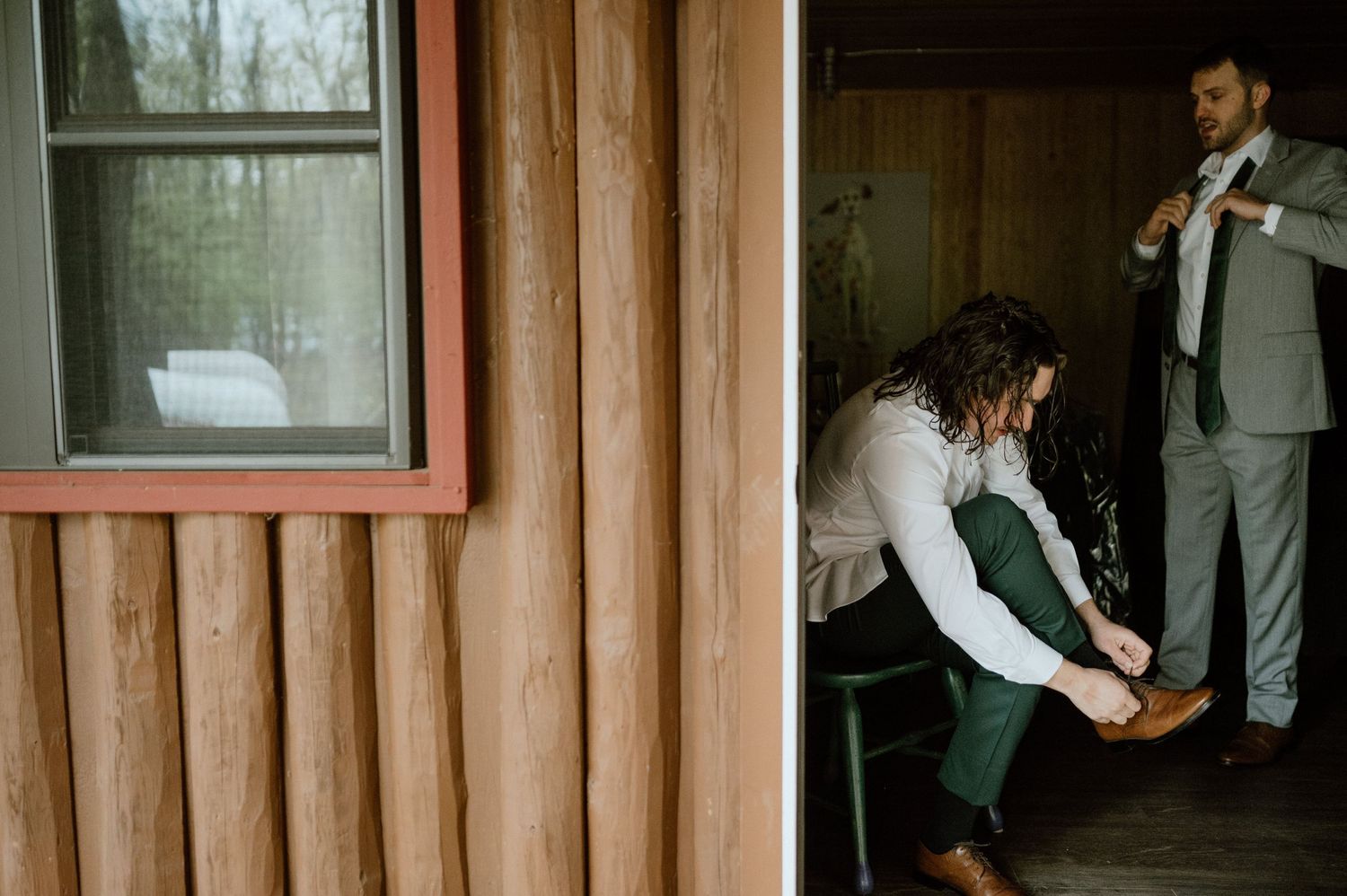 Wedding preparation scene showing final adjustments being made in a wooden cabin interior.