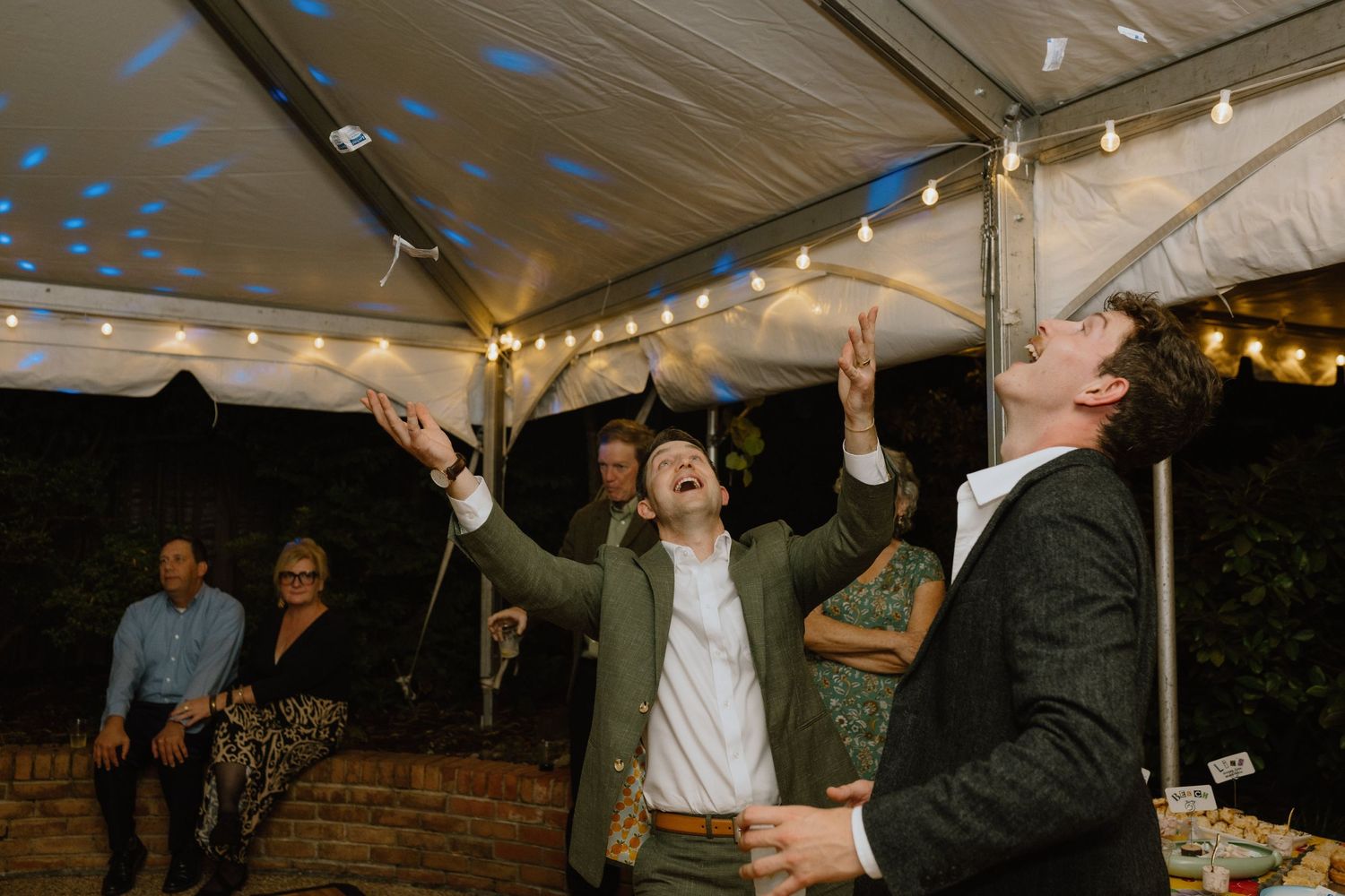 Wedding celebration under tent with string lights and blue spotlights.