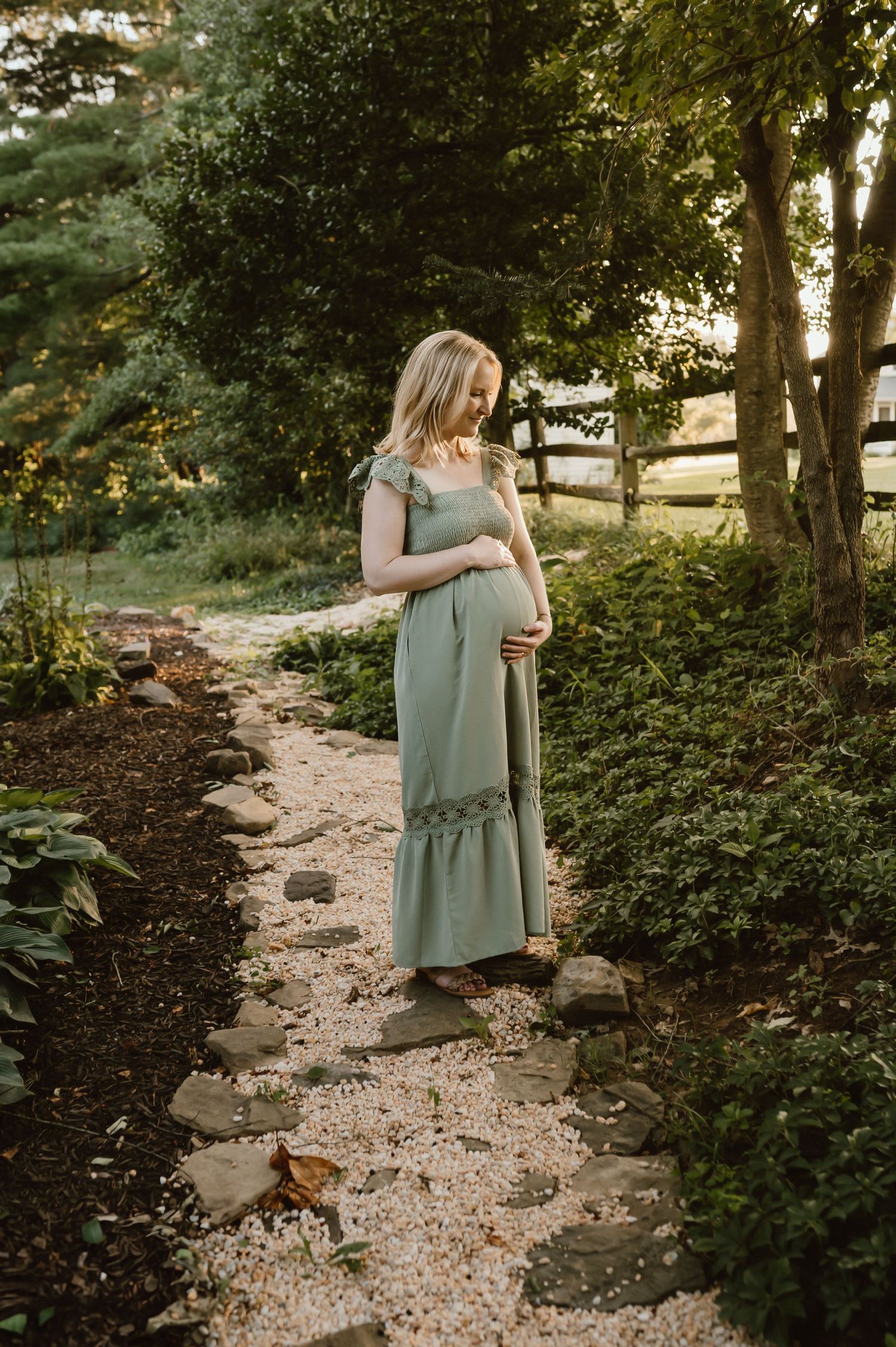 Woman in sage dress stands on garden path during golden hour.
