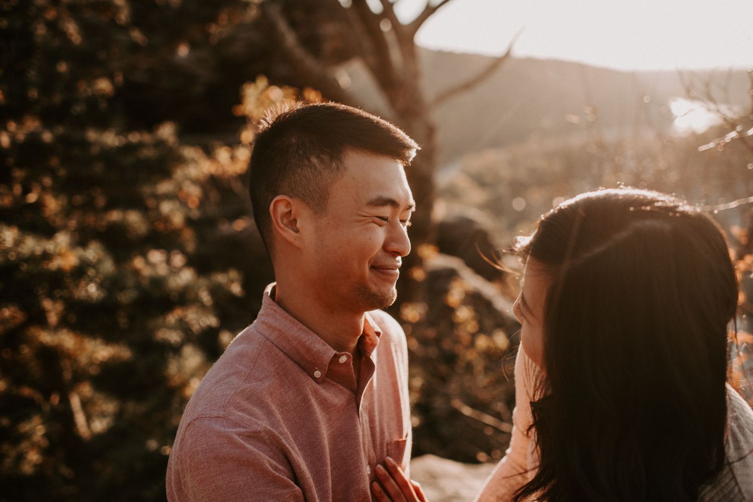 Warm sunset light illuminates couple sharing intimate moment on mountain overlook.