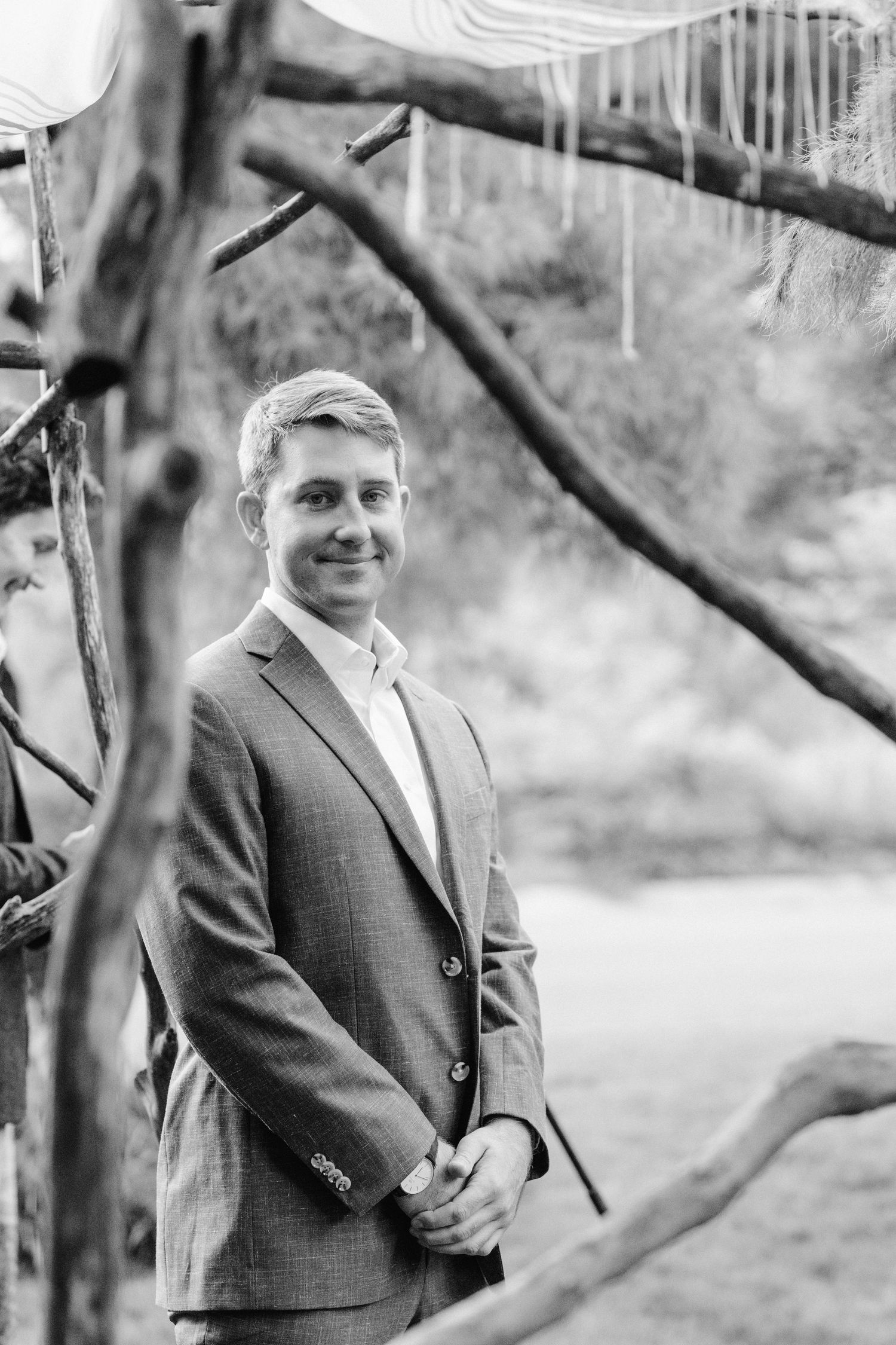 Portrait of a suited gentleman framed by tree branches in a garden setting.