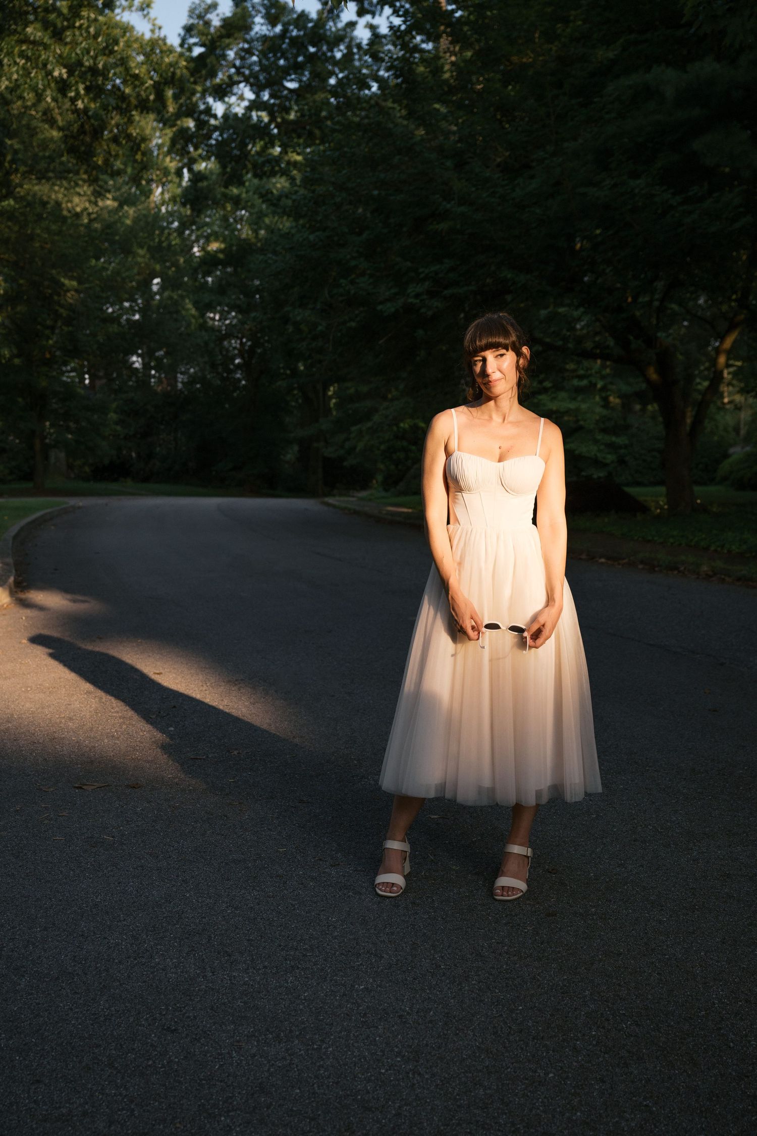 A flowing white dress catches evening sunlight on an outdoor path.