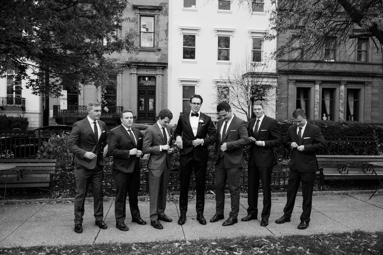Groomsmen in formal attire lined up in front of historic brick building.