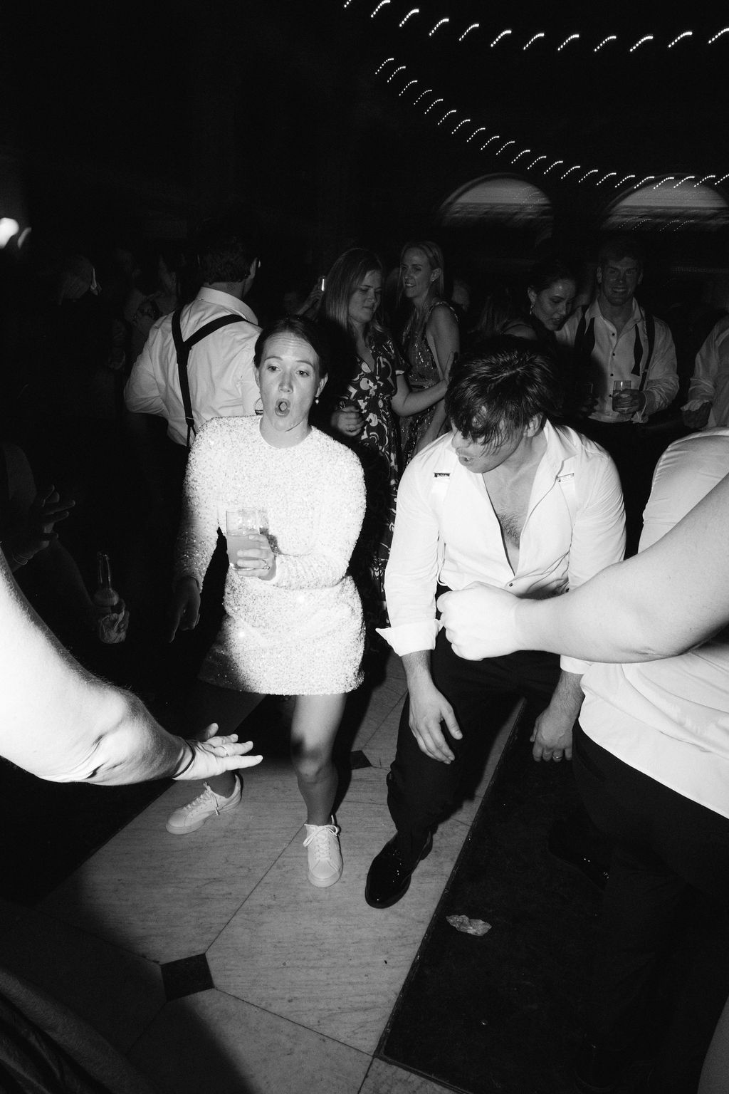 Low-angle shot of wedding guests dancing on illuminated dance floor.