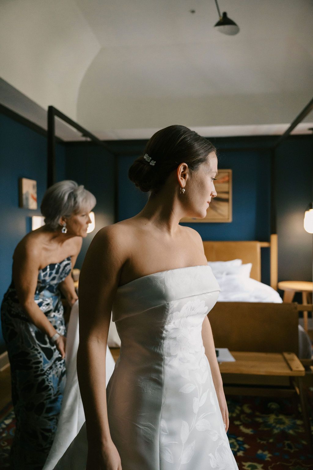Bride in white strapless wedding dress getting ready in a room with dark blue walls.