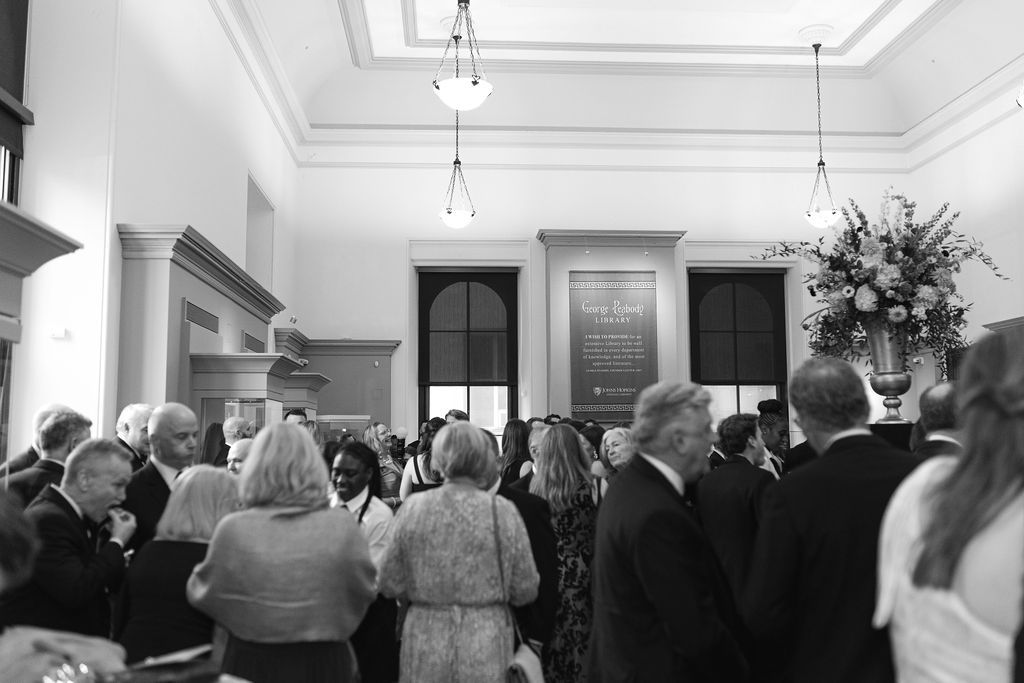 A crowd gathers inside an elegant venue with high ceilings and ornate architectural details at George Peabody Library Wedding in Baltimore