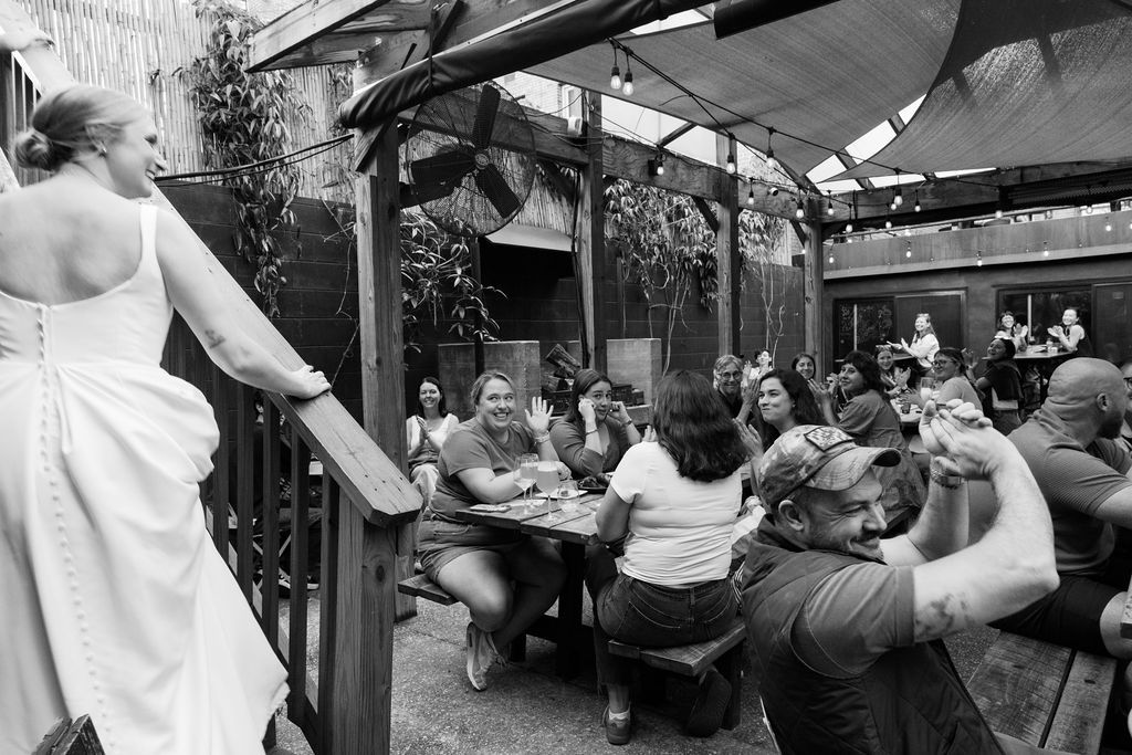 Outdoor wedding reception with guests seated at tables under string lights.