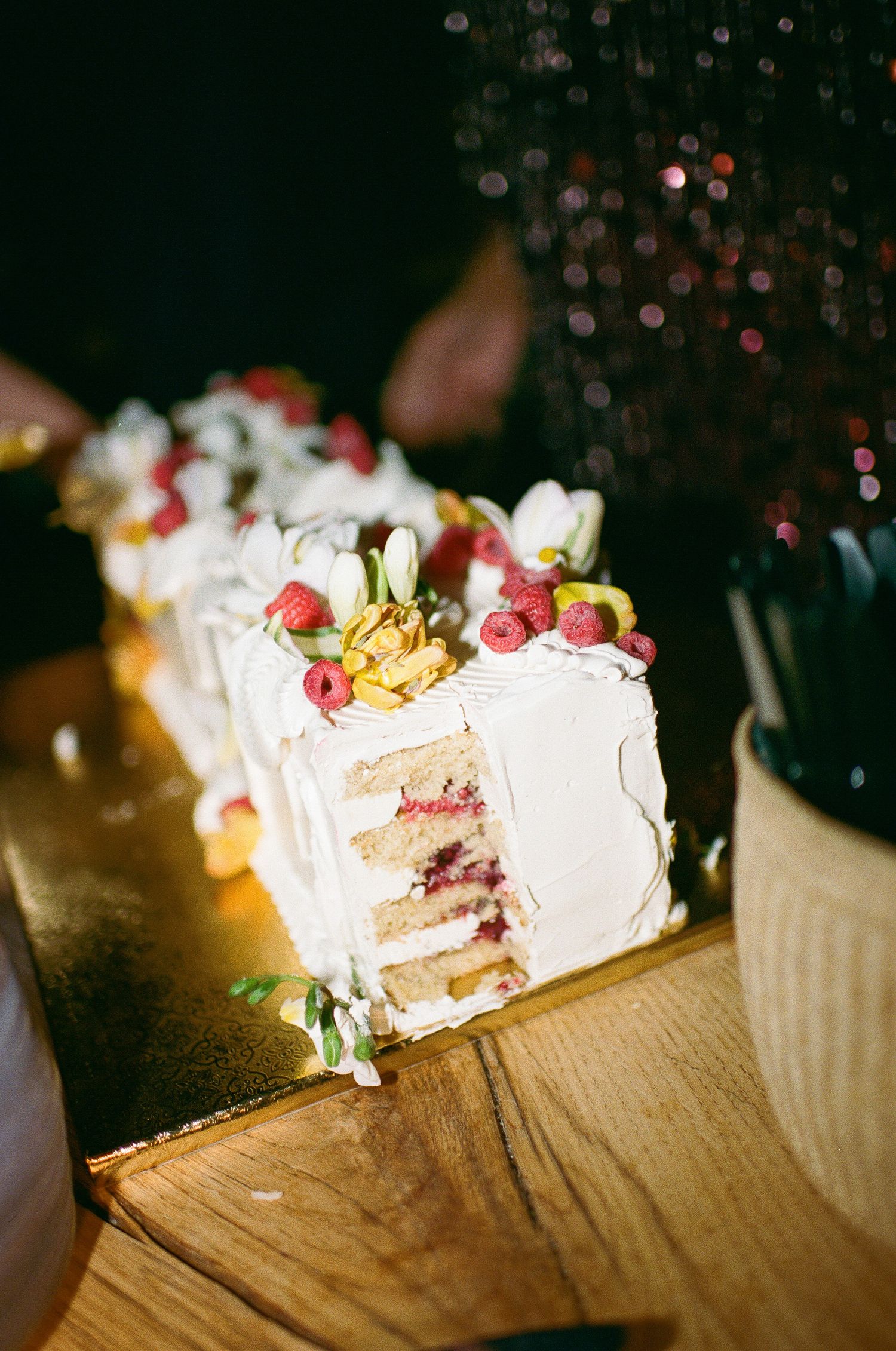 Slices of layered cream cake decorated with fresh raspberries and gold accents on a wooden surface.