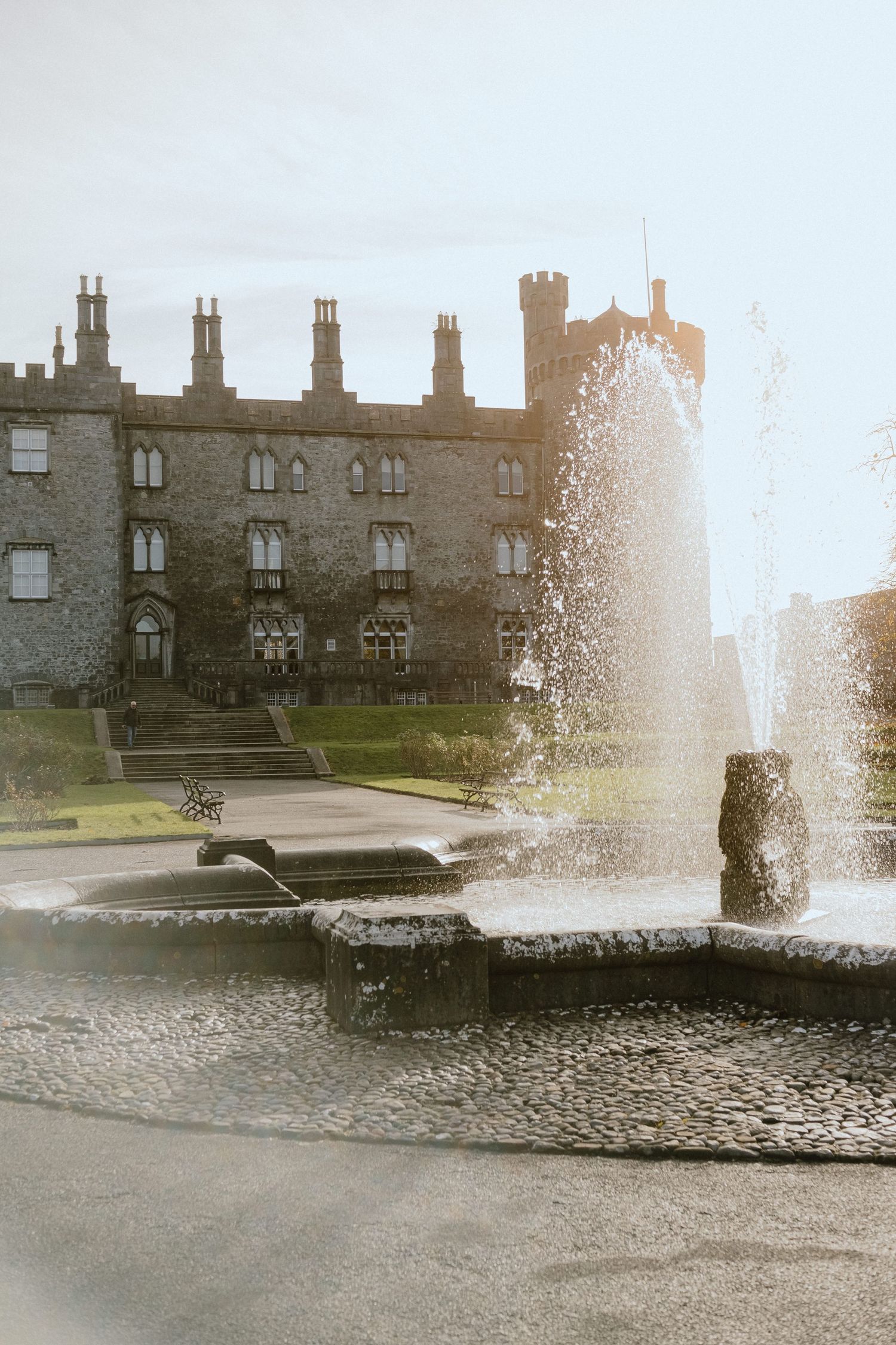Stone castle with fountains spraying water in front of Gothic architecture.