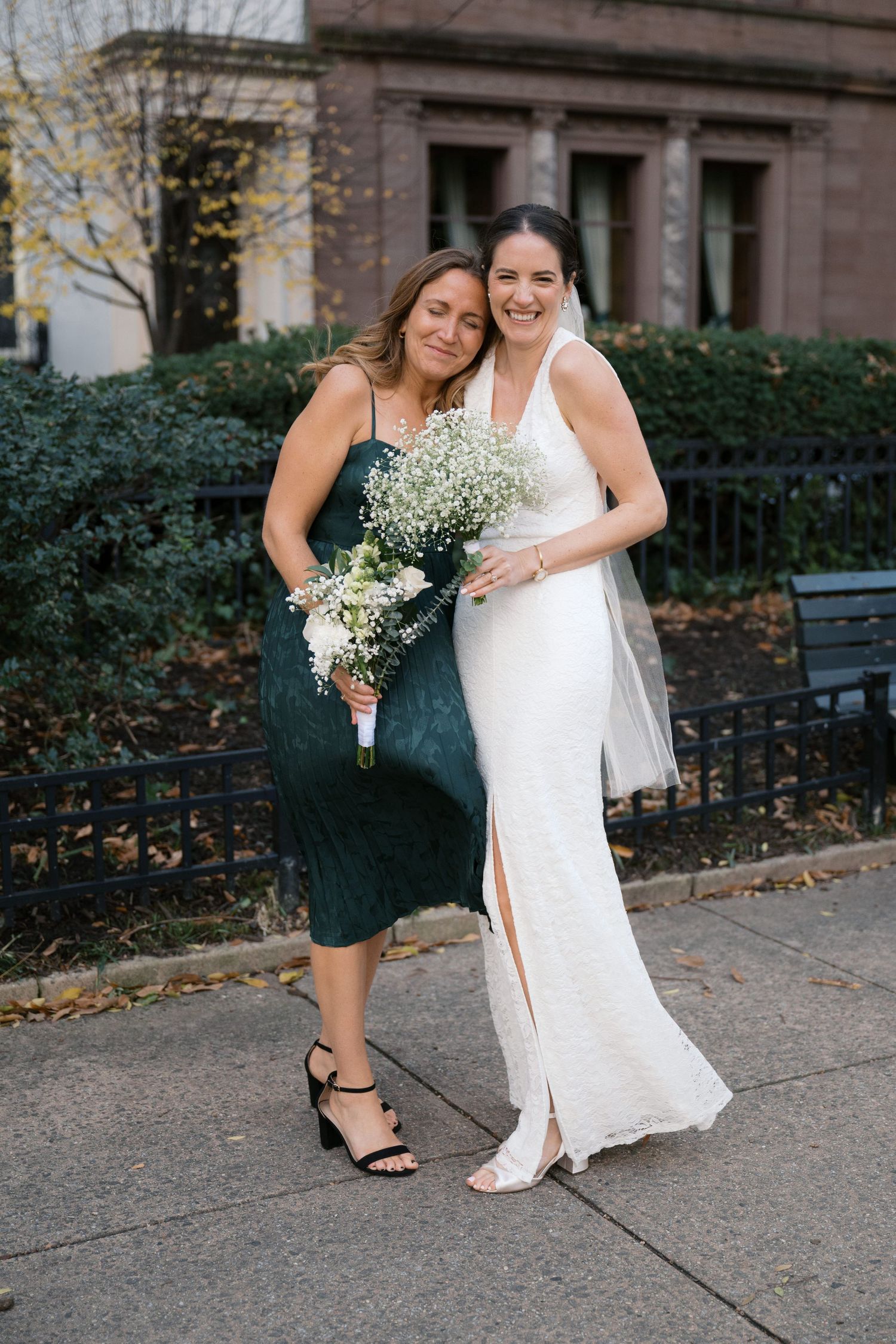 Bridesmaid in navy dress and bride with baby's breath bouquet pose together outdoors.