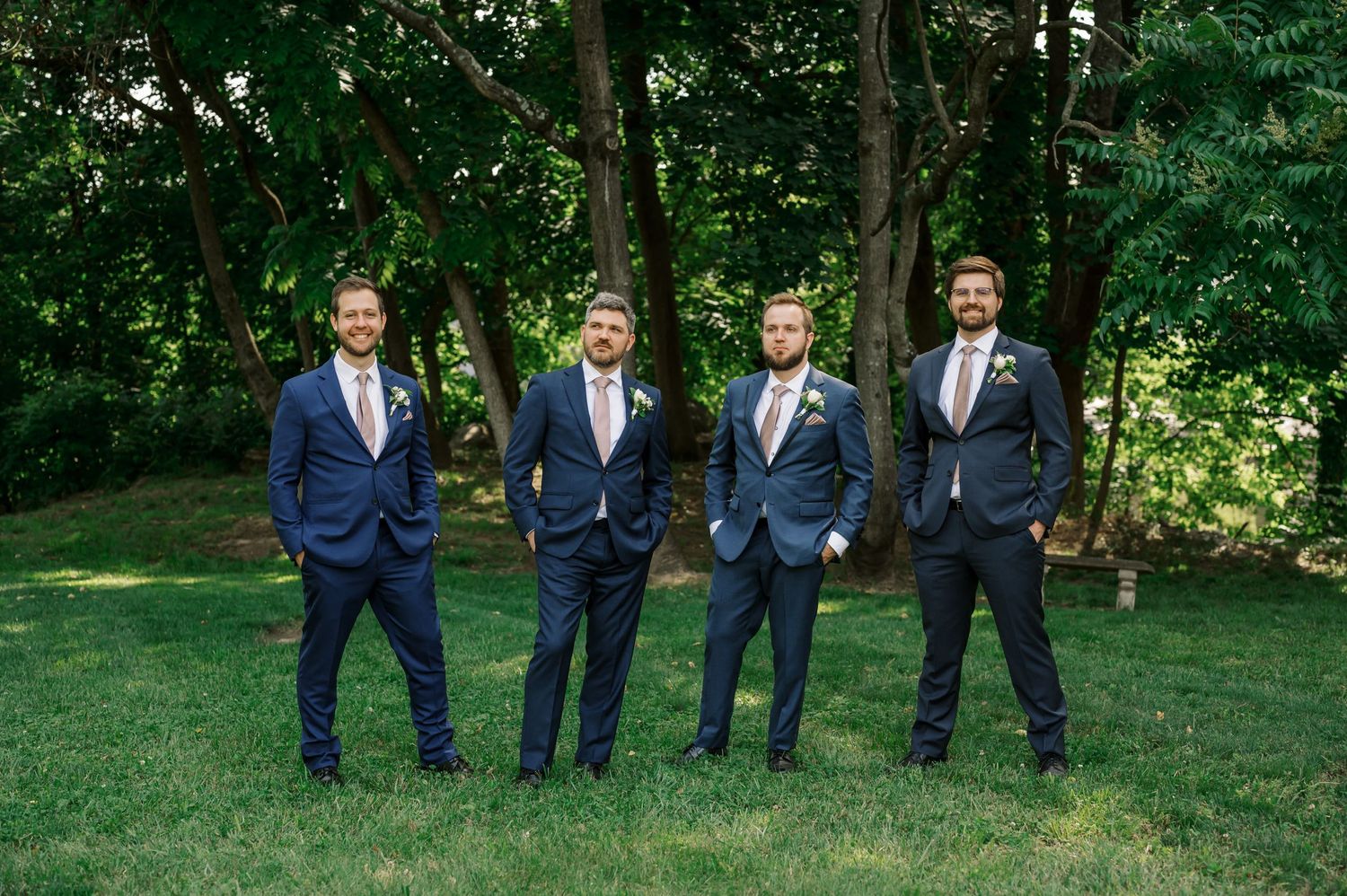 Groomsmen in navy suits posing on lawn in front of trees.