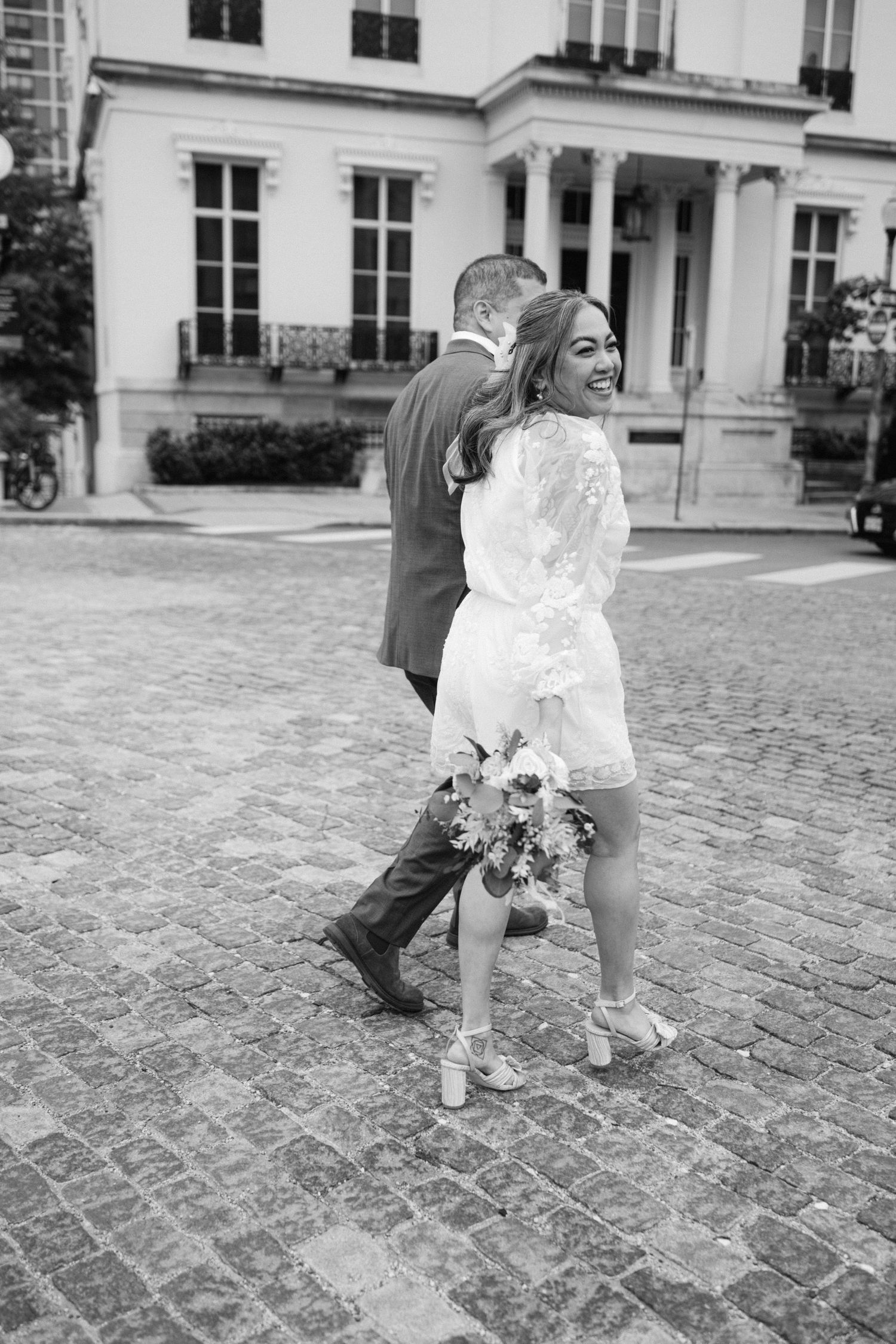 A couple walks on cobblestone streets with a beautiful historic building in the background.