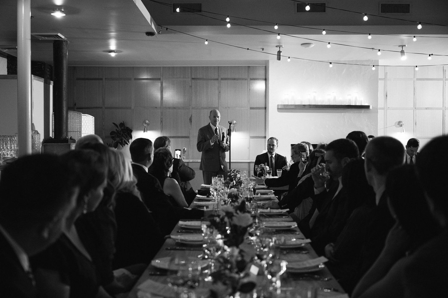 Black and white photo of guests seated at a long dinner table during a formal event.
