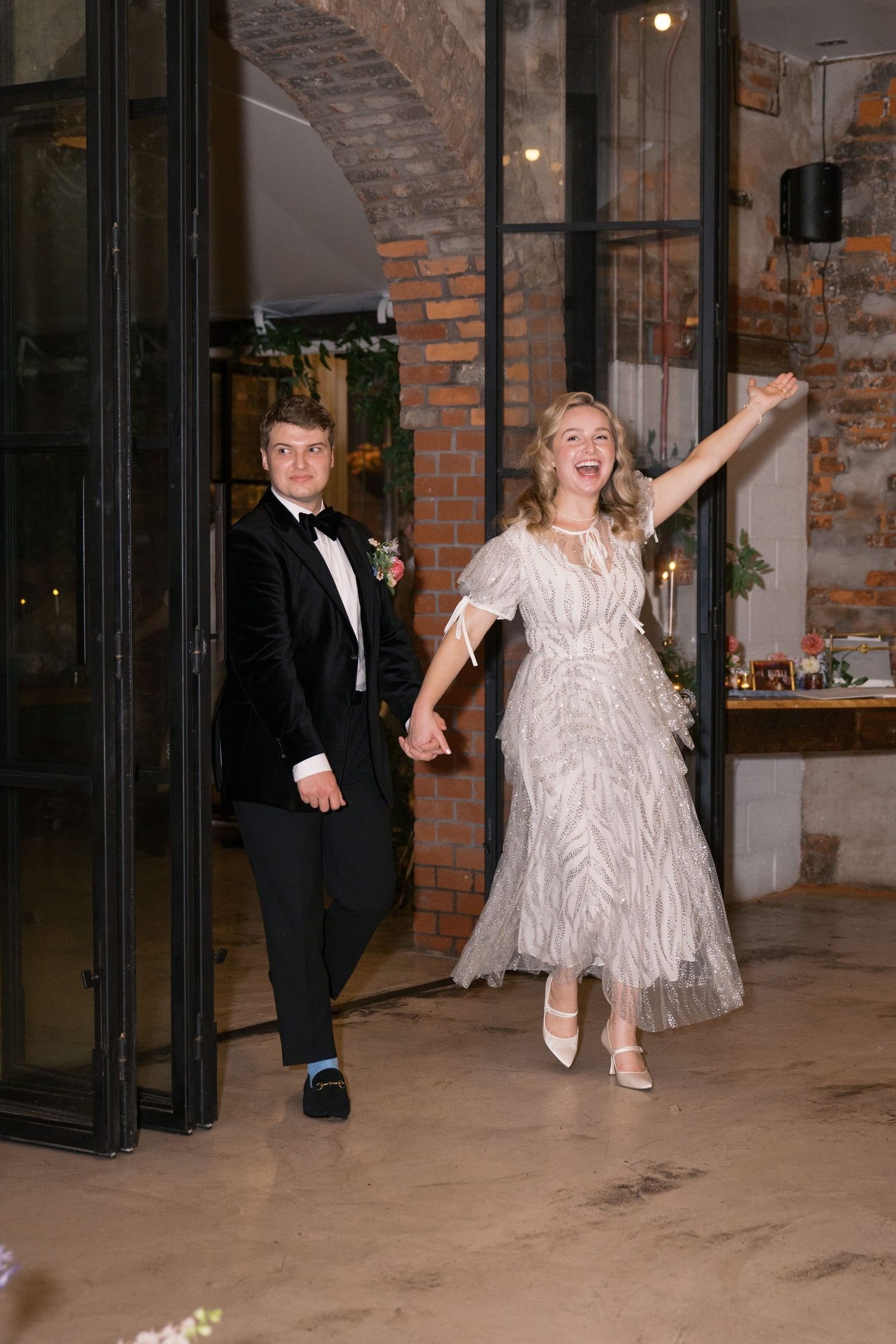 Wedding couple making a grand entrance into their reception venue with exposed brick walls.