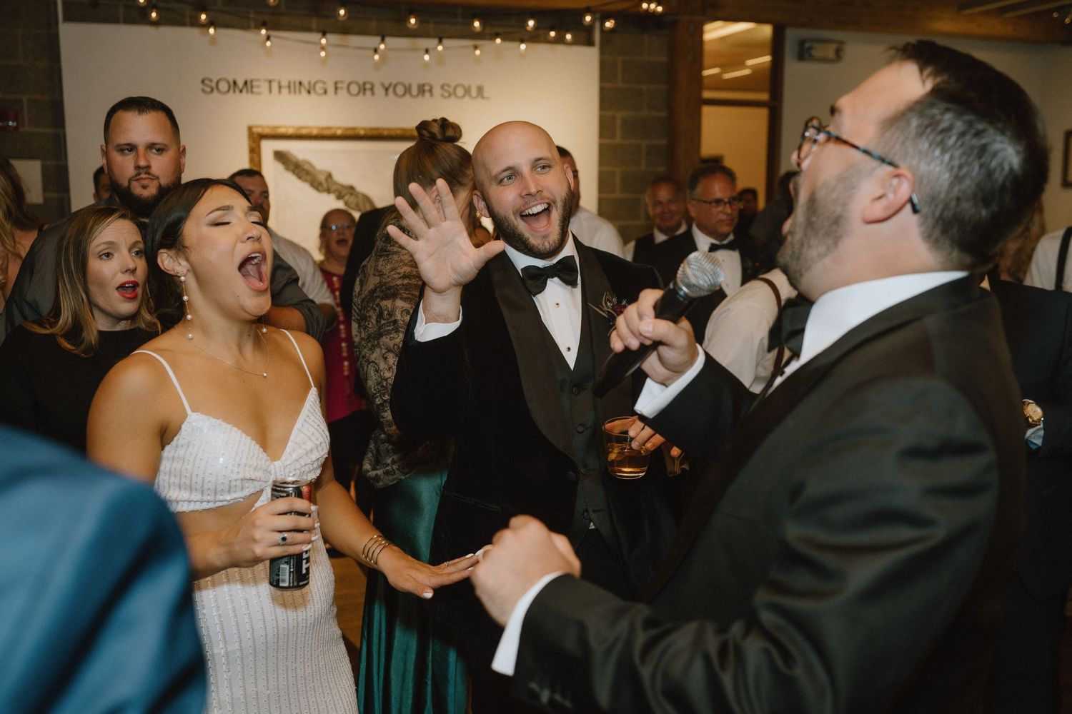 Wedding guests share an energetic moment of laughter and celebration at an indoor reception.