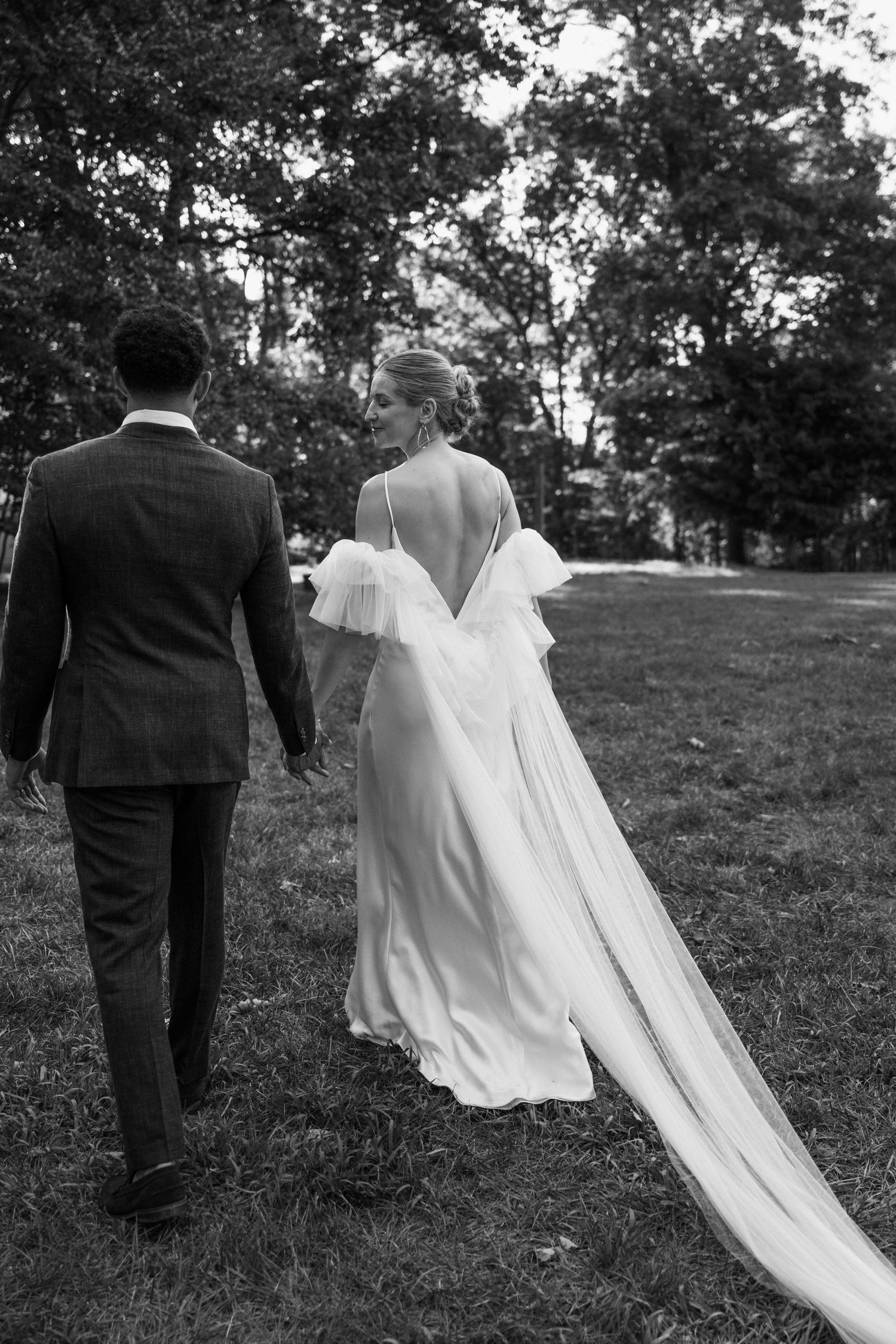 Wedding couple walks through a garden, with bride's elegant dress and train flowing behind them.