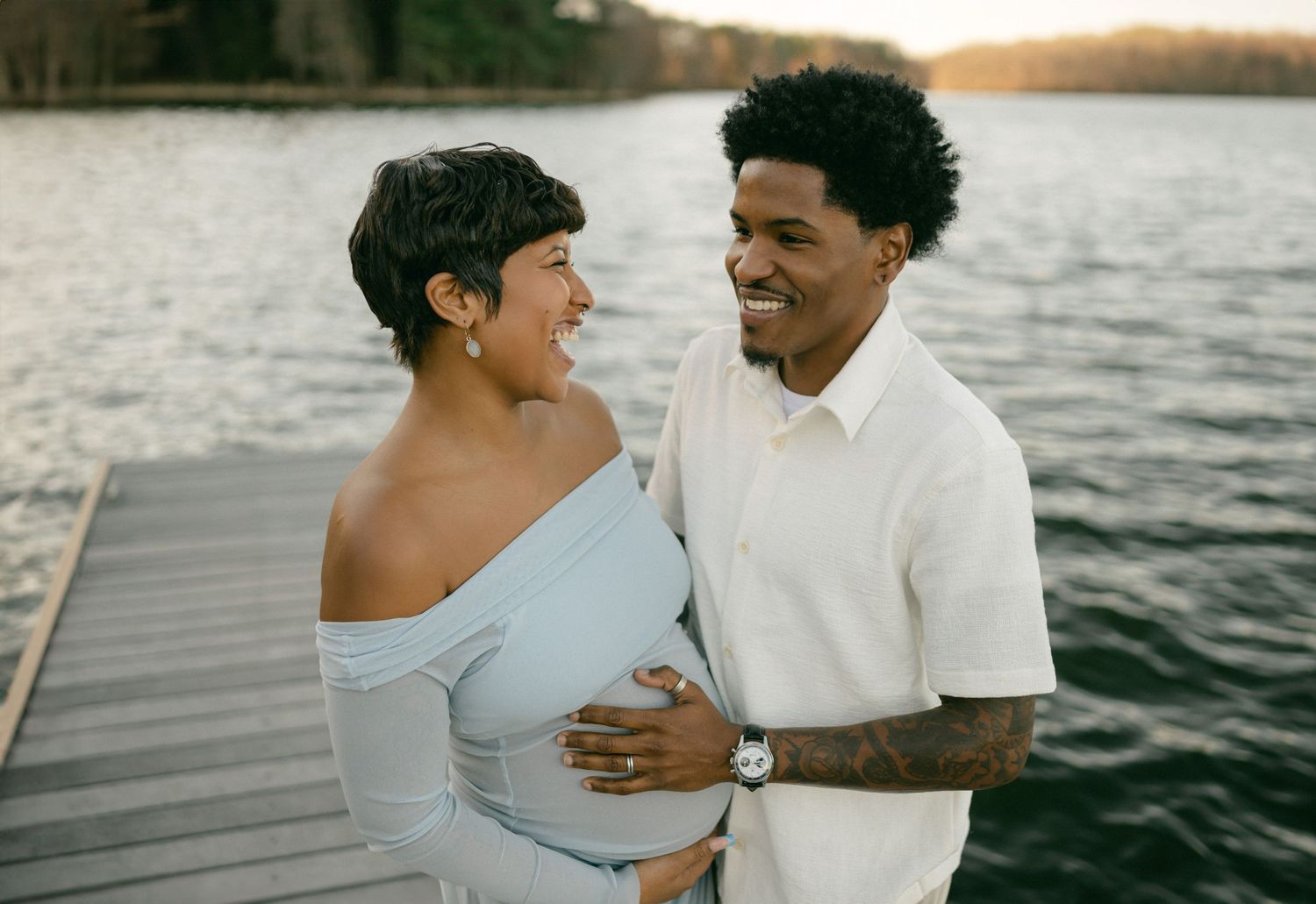 pregnant couple on dock laughing mans hand on baby bump