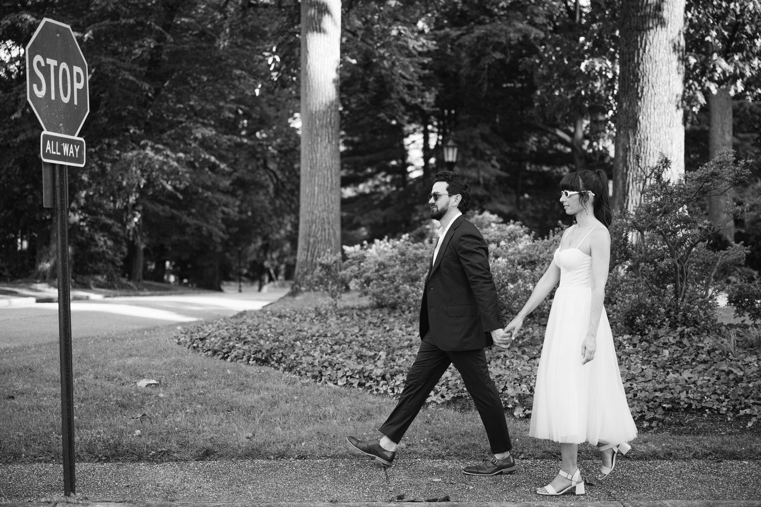 A couple walks past a stop sign on a quiet suburban street in formal attire.