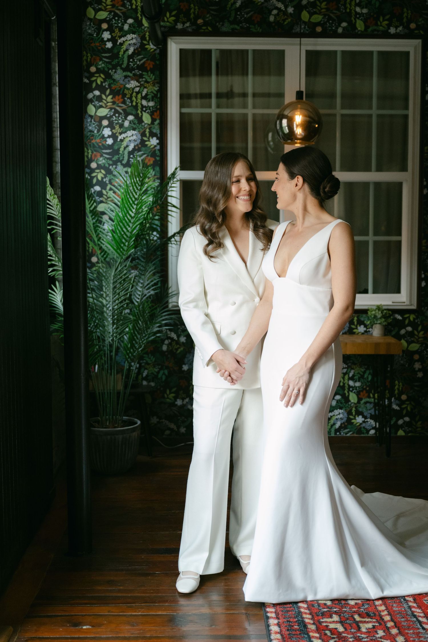 Two people in white attire sharing an intimate moment in a room with indoor plants.