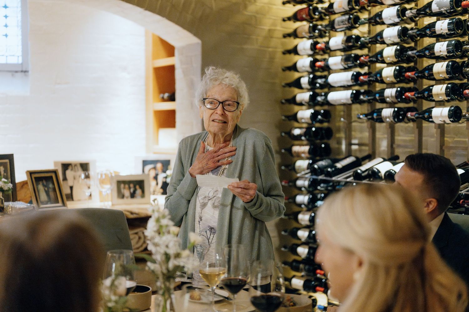 A wedding reception speech being given in front of a wall of wine bottles.