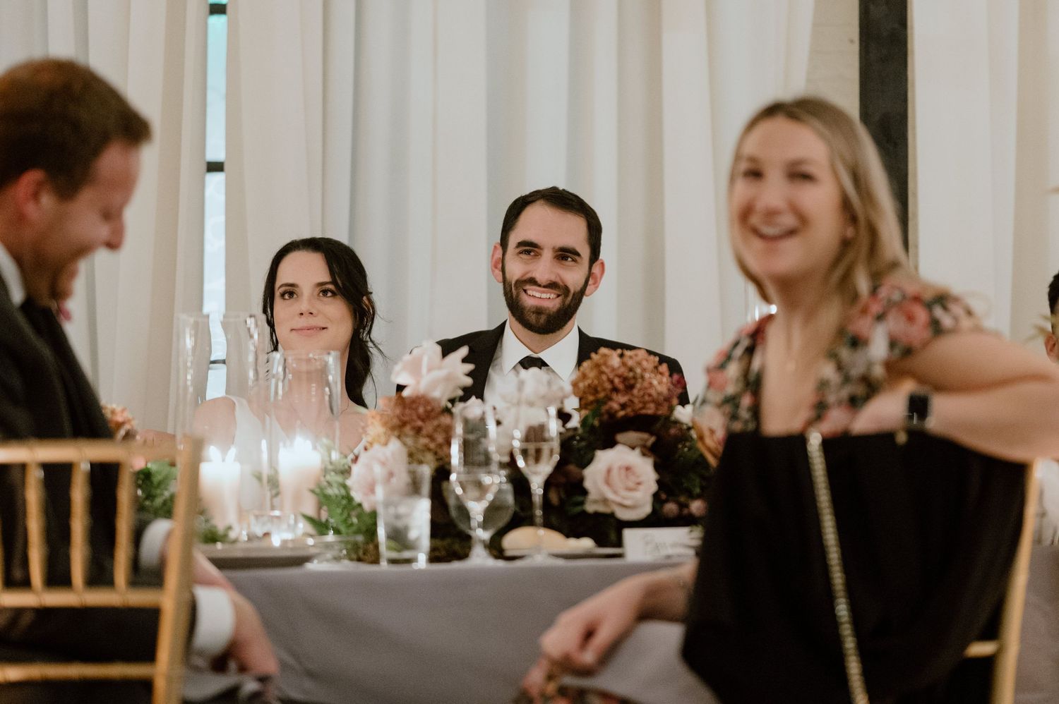 Wedding reception candid moment showing guests laughing at dinner table.