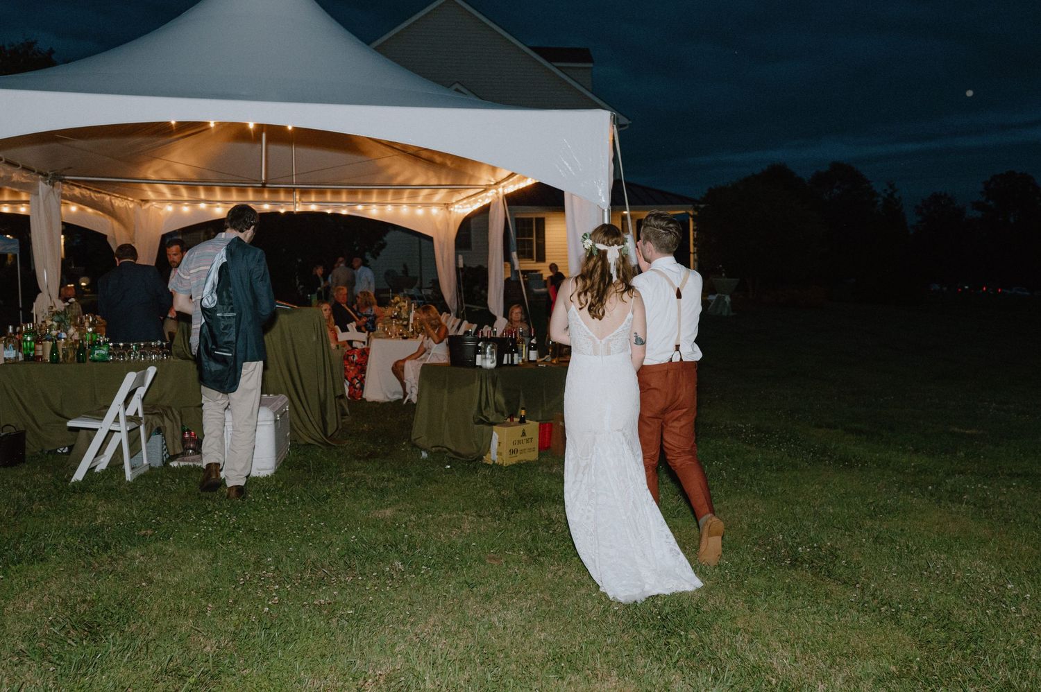 A couple dances together under a white tent at an outdoor evening wedding reception.