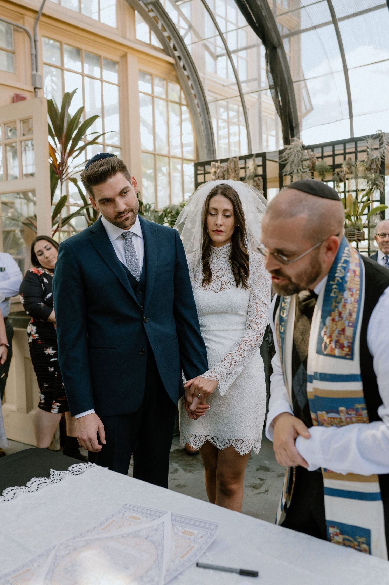 A couple participates in Jewish wedding ceremony with rabbi in front of marriage contract.