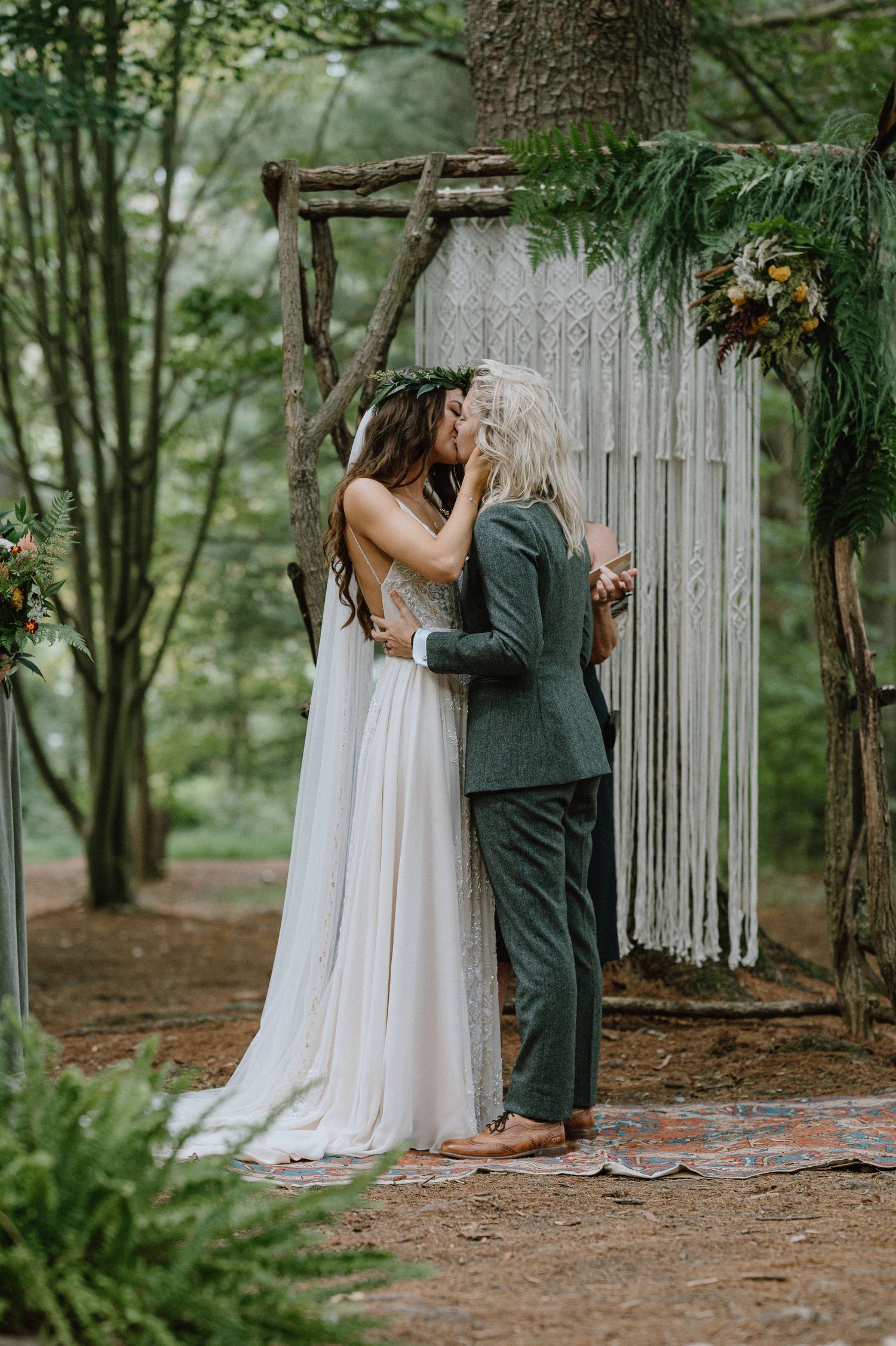 Couple shares their first kiss under a macrame backdrop during their forest wedding ceremony.