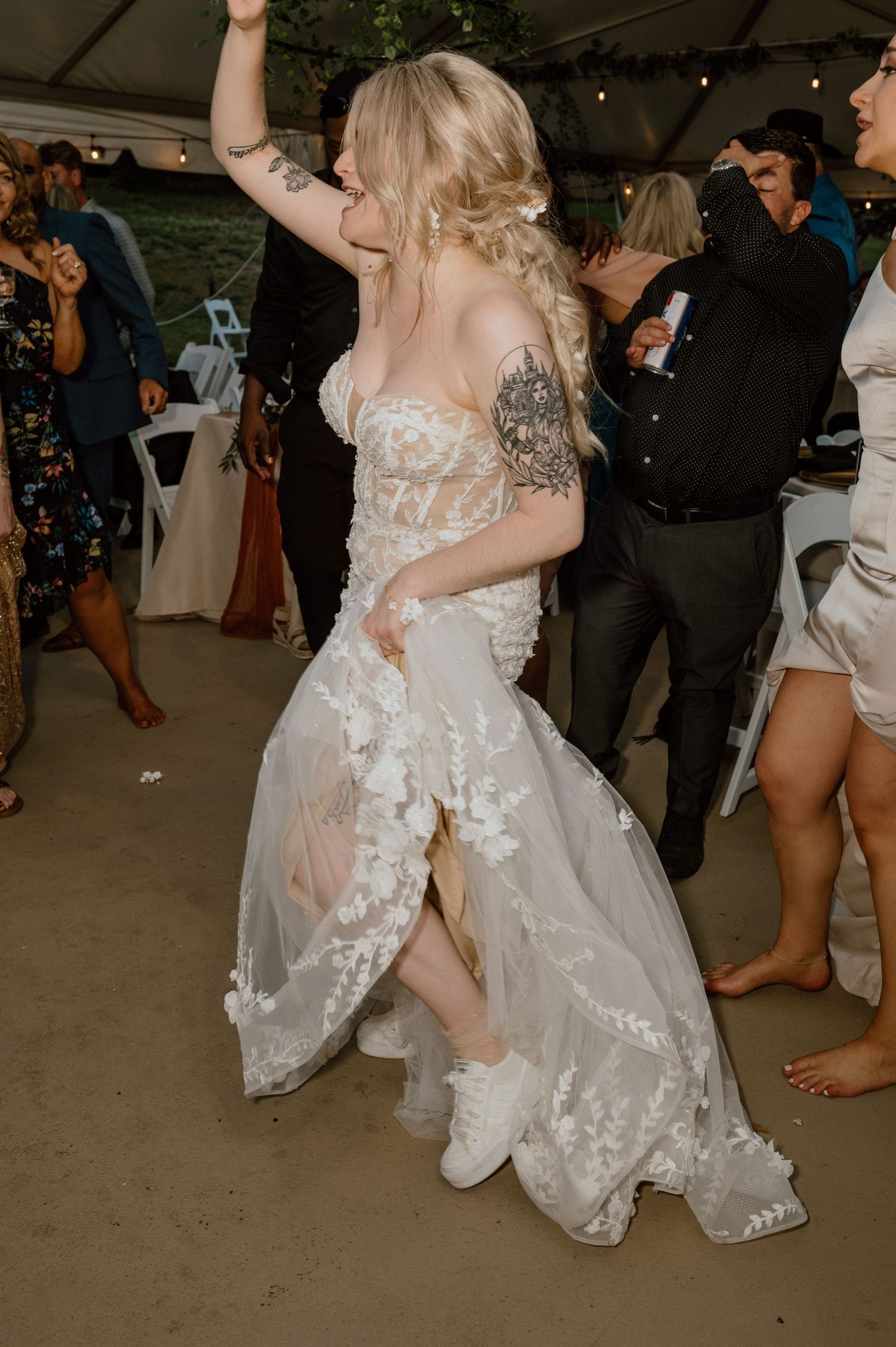 Bride in lacy white dress dancing and celebrating at a wedding reception under a tent.