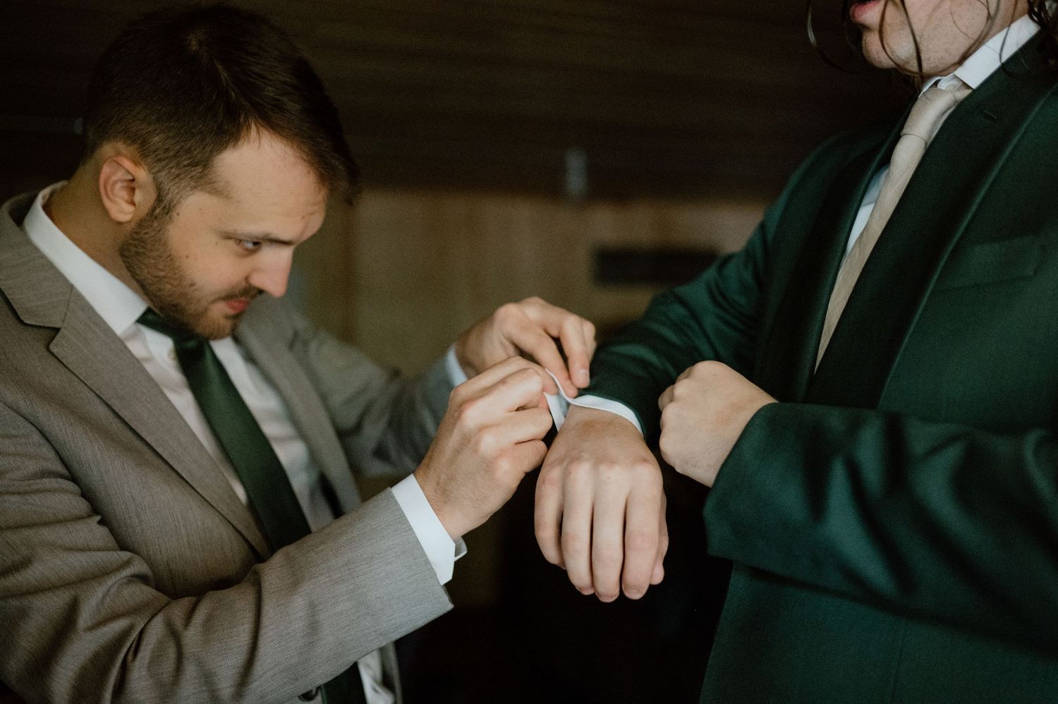 Wedding preparations showing a man in suit helping another with formal attire adjustments.