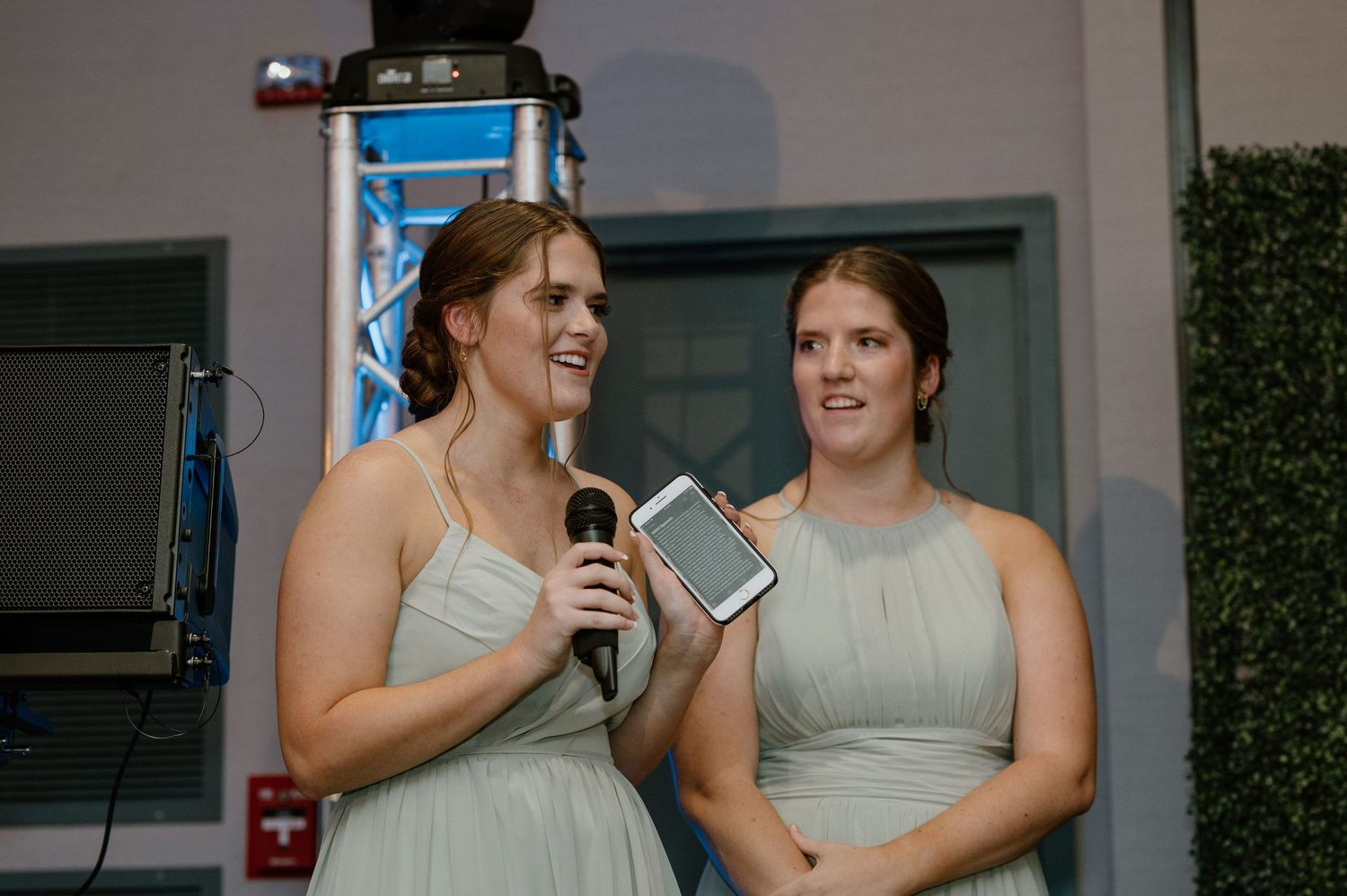 Two bridesmaids in light colored dresses give an emotional speech during the wedding reception.