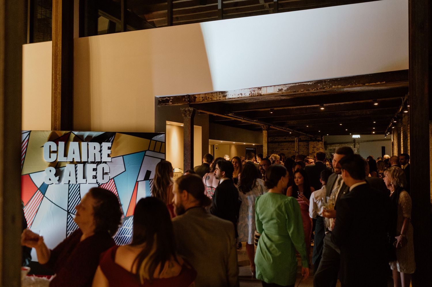 Dark indoor venue with illuminated signage and crowd of people mingling at an event.