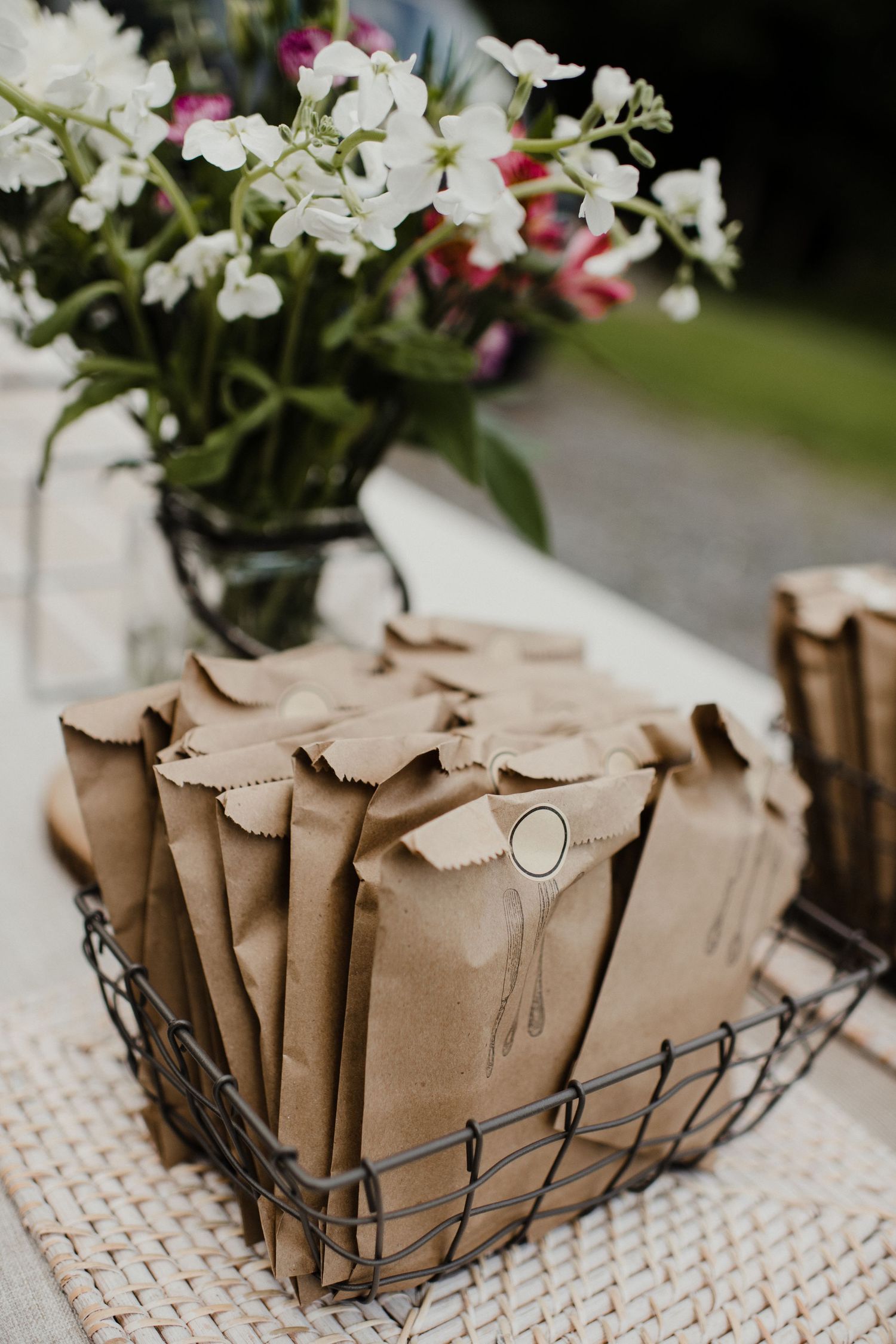 Brown paper favor bags arranged in wire basket with white floral centerpiece.