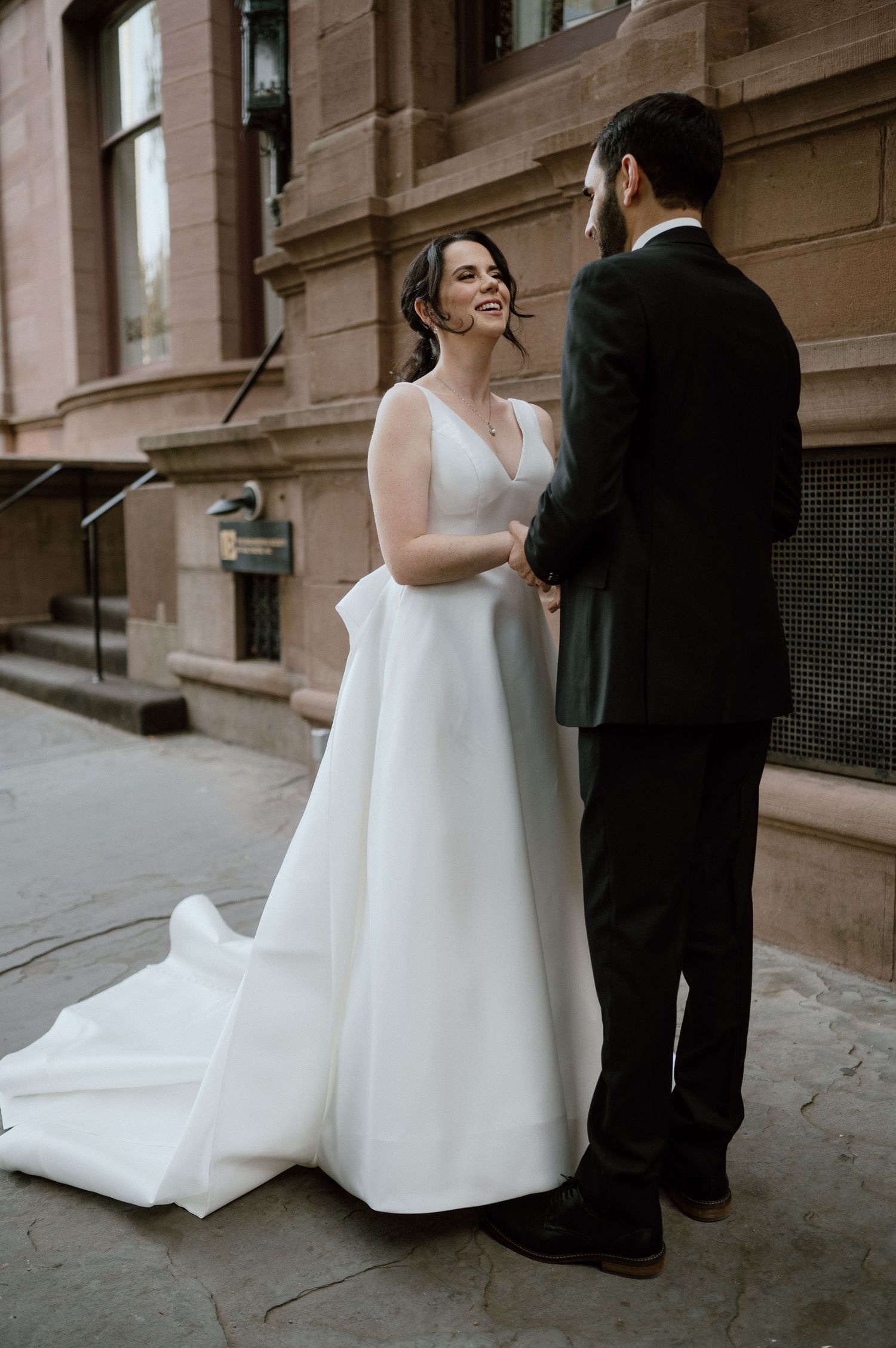A couple shares an intimate moment on their wedding day in front of a brownstone building.