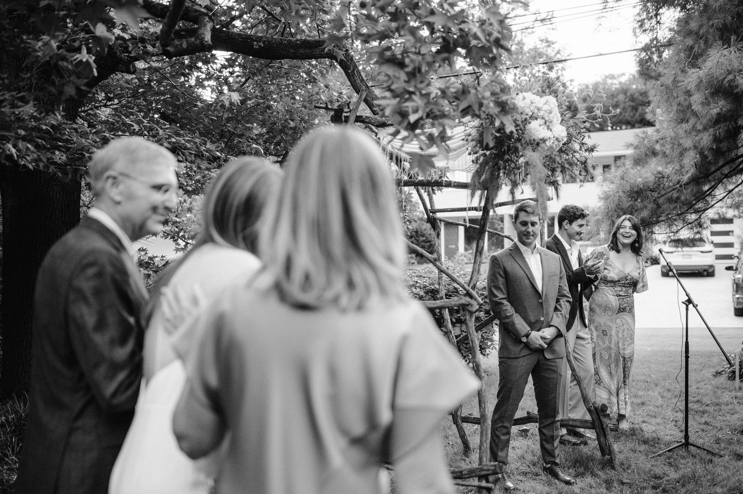 Black and white candid photo of wedding guests interacting during an outdoor celebration.