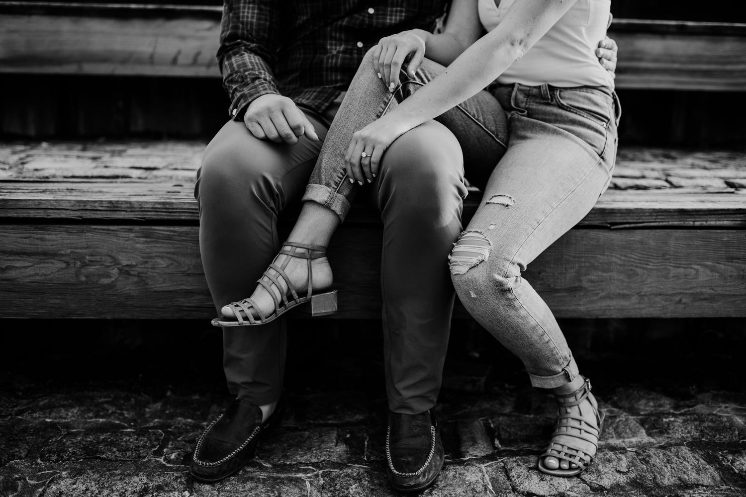 Close-up view of two people sitting together on wooden steps wearing jeans and sandals.