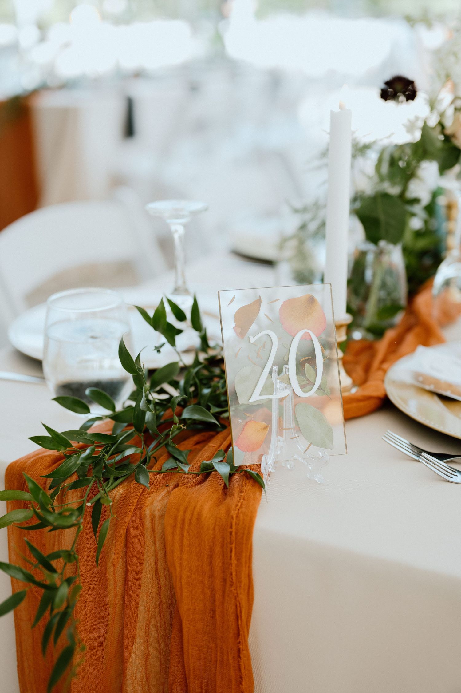 Wedding table setting with orange fabric runner, greenery, and table number twenty.