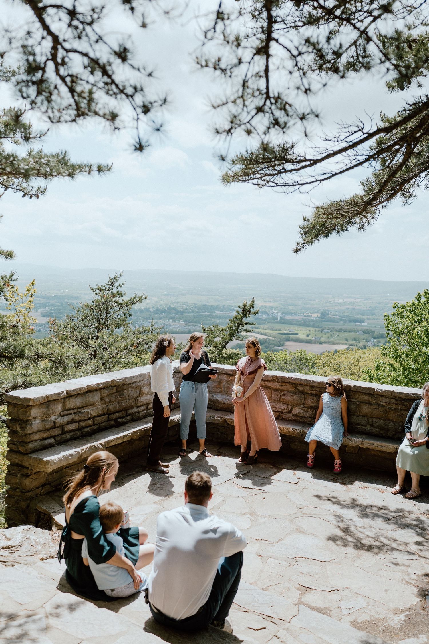 Aerial view of people celebrating at a mountain viewpoint with stone benches.
