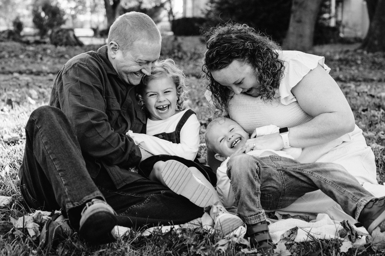 Black and white portrait of family laughing together on blanket outdoors.