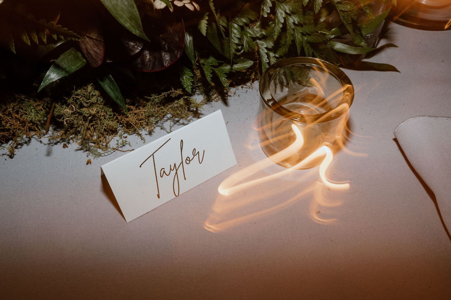Close-up of a place card and floral arrangement with neon lighting at a wedding reception.