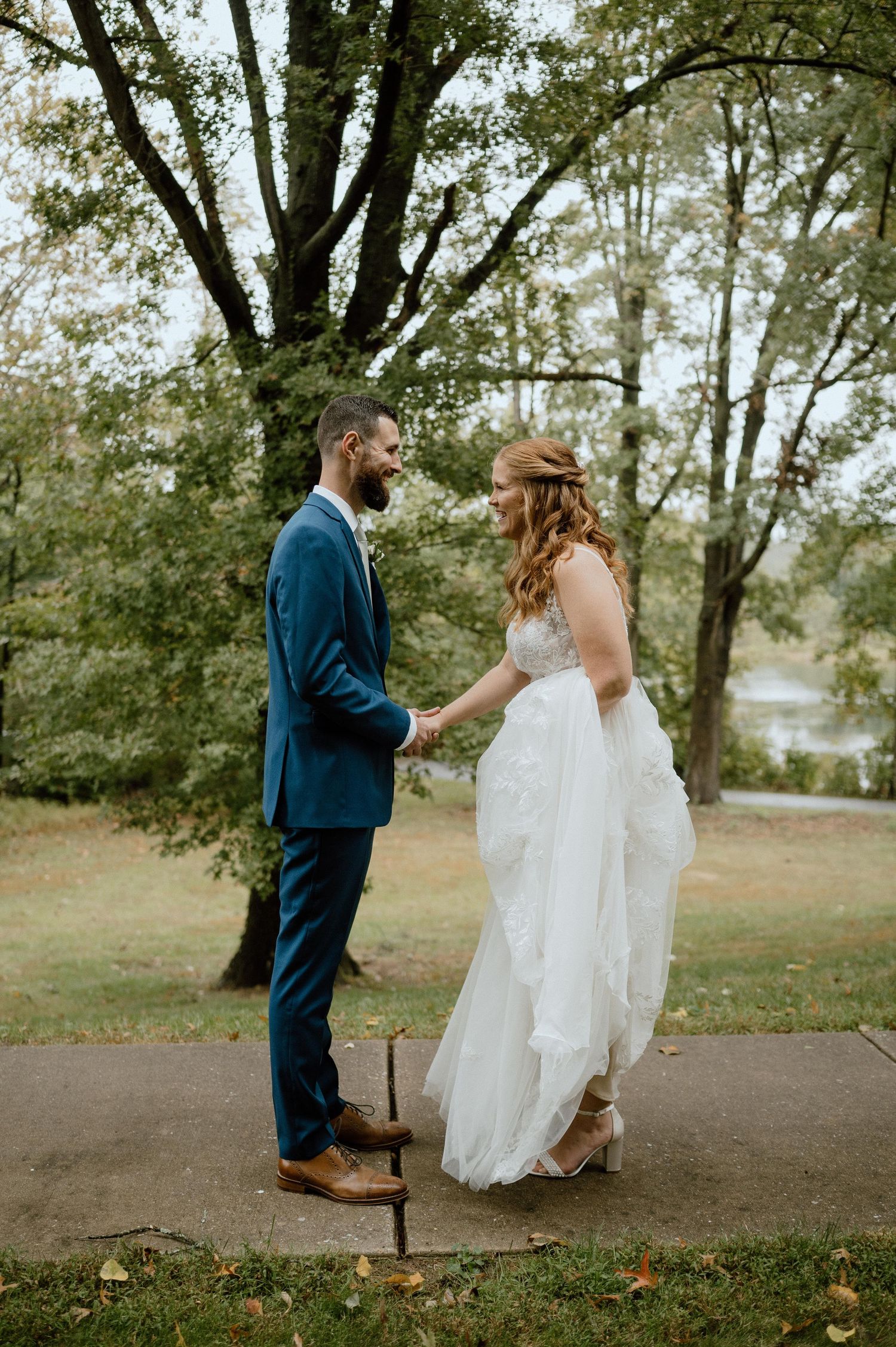 Romantic first look moment between couple on pathway surrounded by autumn trees.