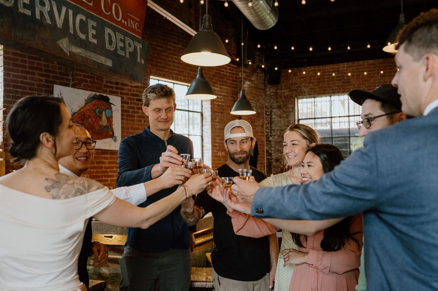 Group toasting with drinks in an industrial-style distillery space.