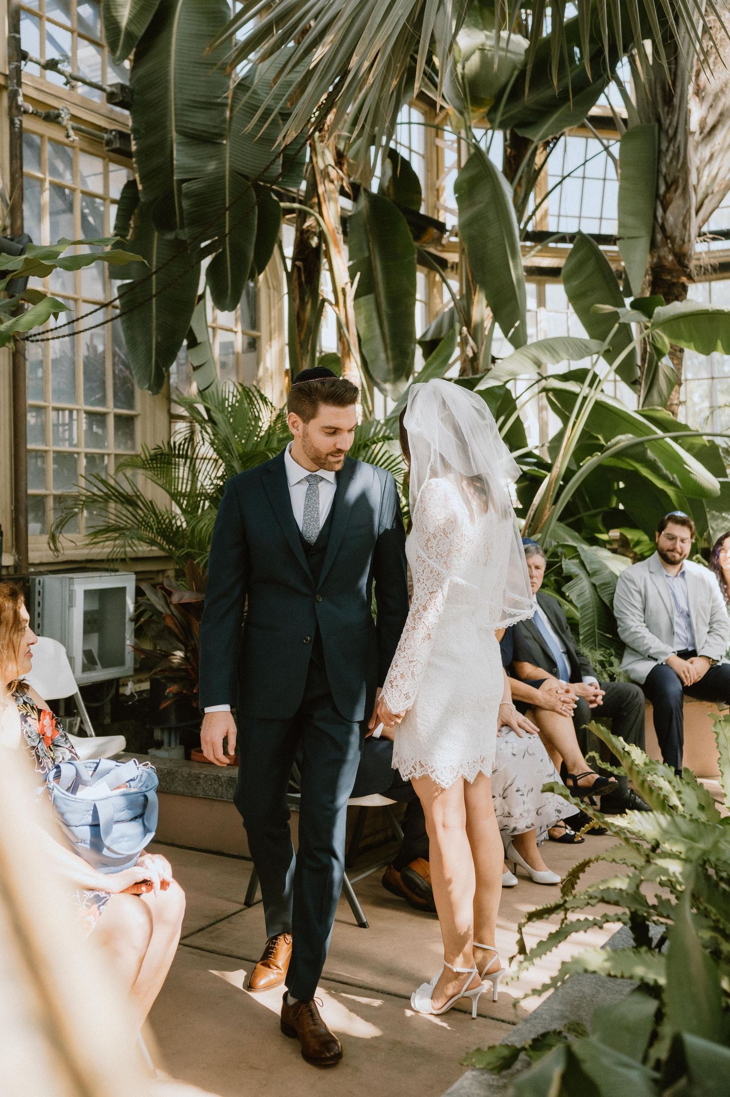 A couple walks together through a botanical garden greenhouse during their wedding celebration.