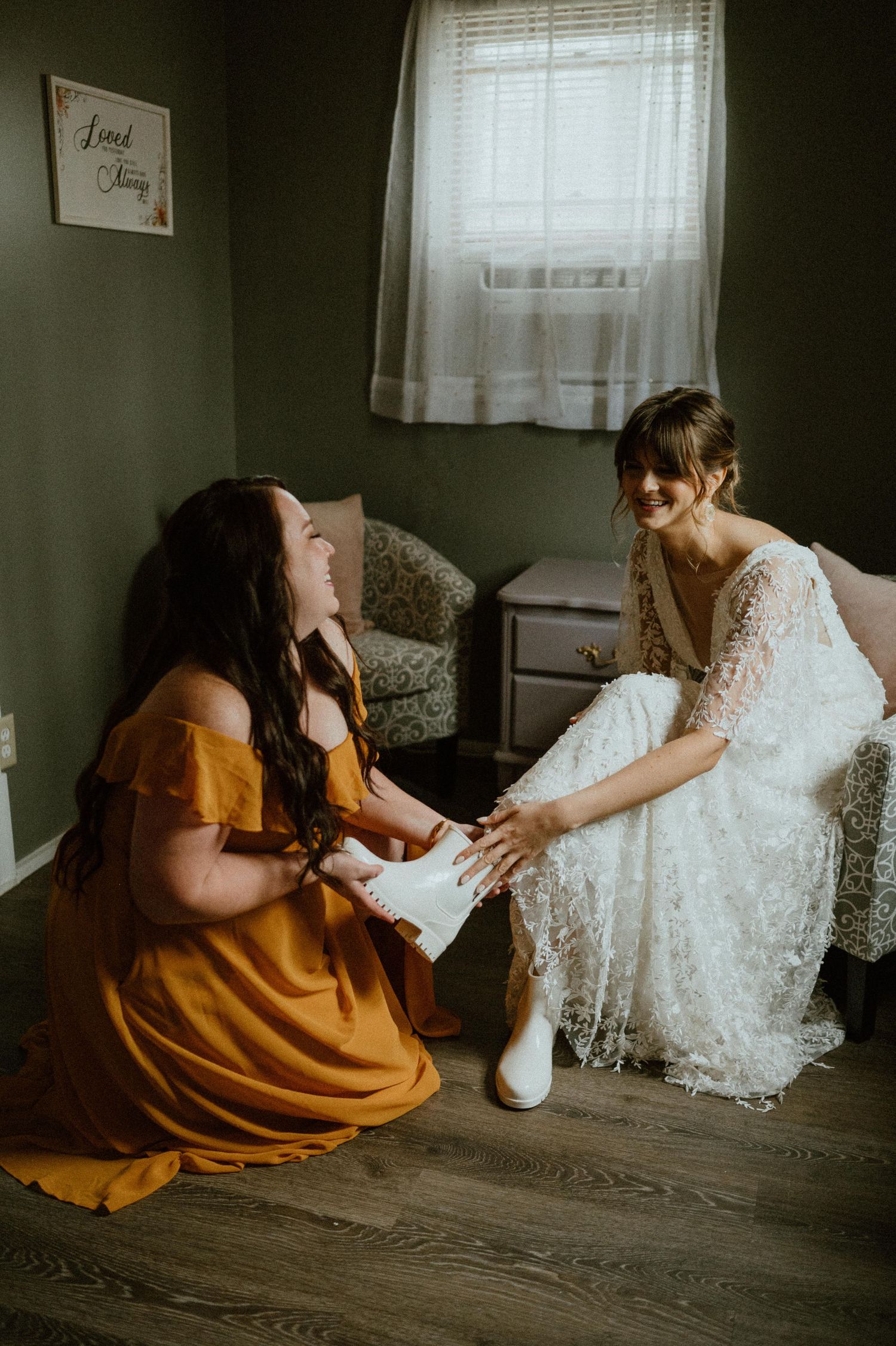 A heartfelt moment of wedding preparation as two people share a laugh while looking at a white lace dress.