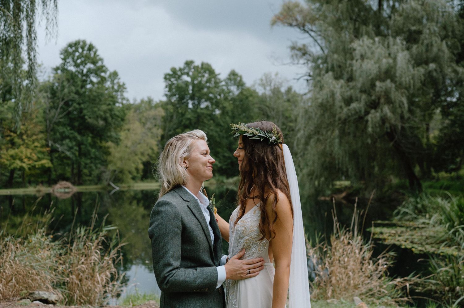 A romantic wedding moment by a tranquil pond with weeping willows and natural scenery in the background.